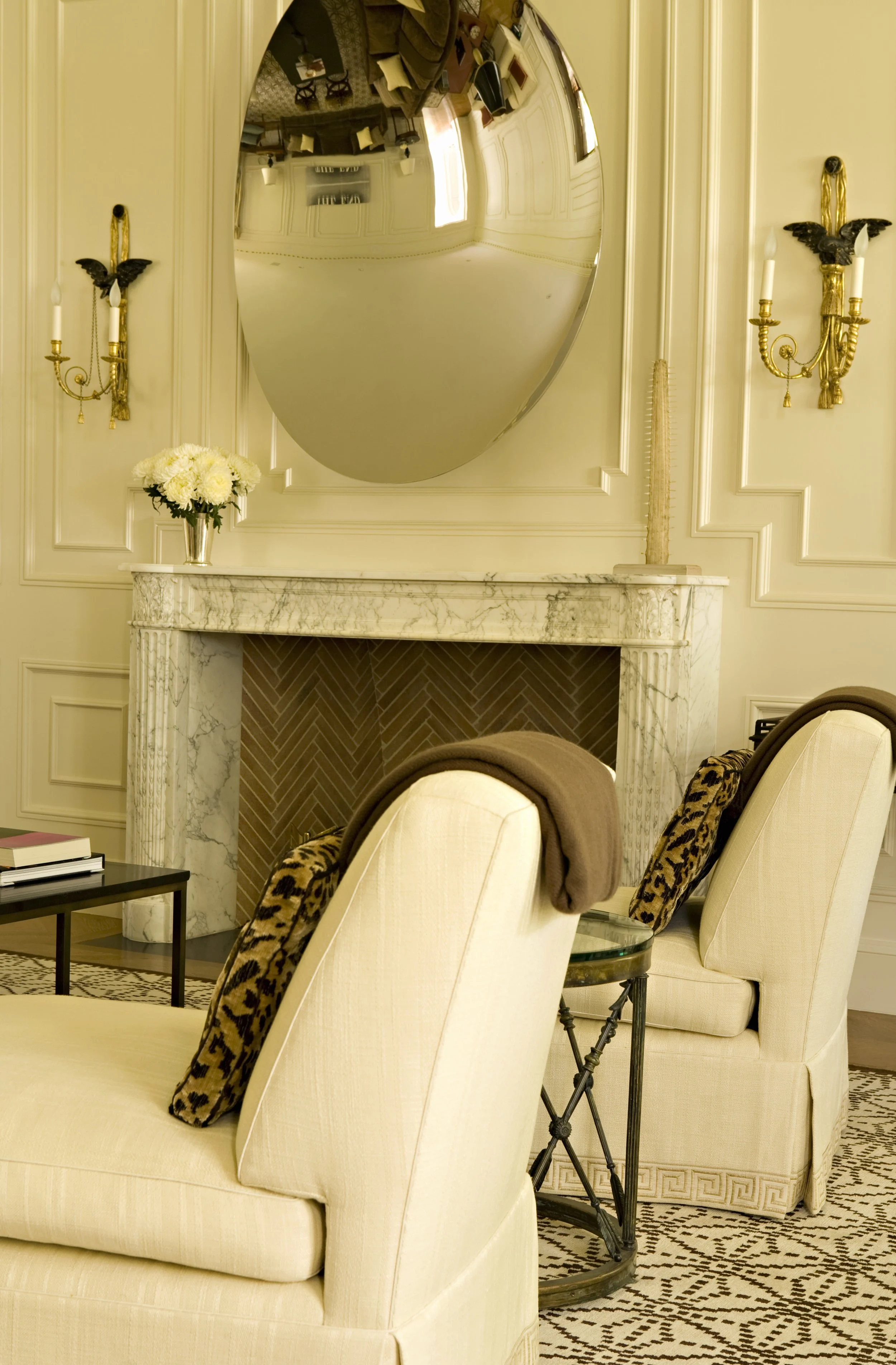 Marble fireplace with chevron brick, cream chairs and leopard pillows