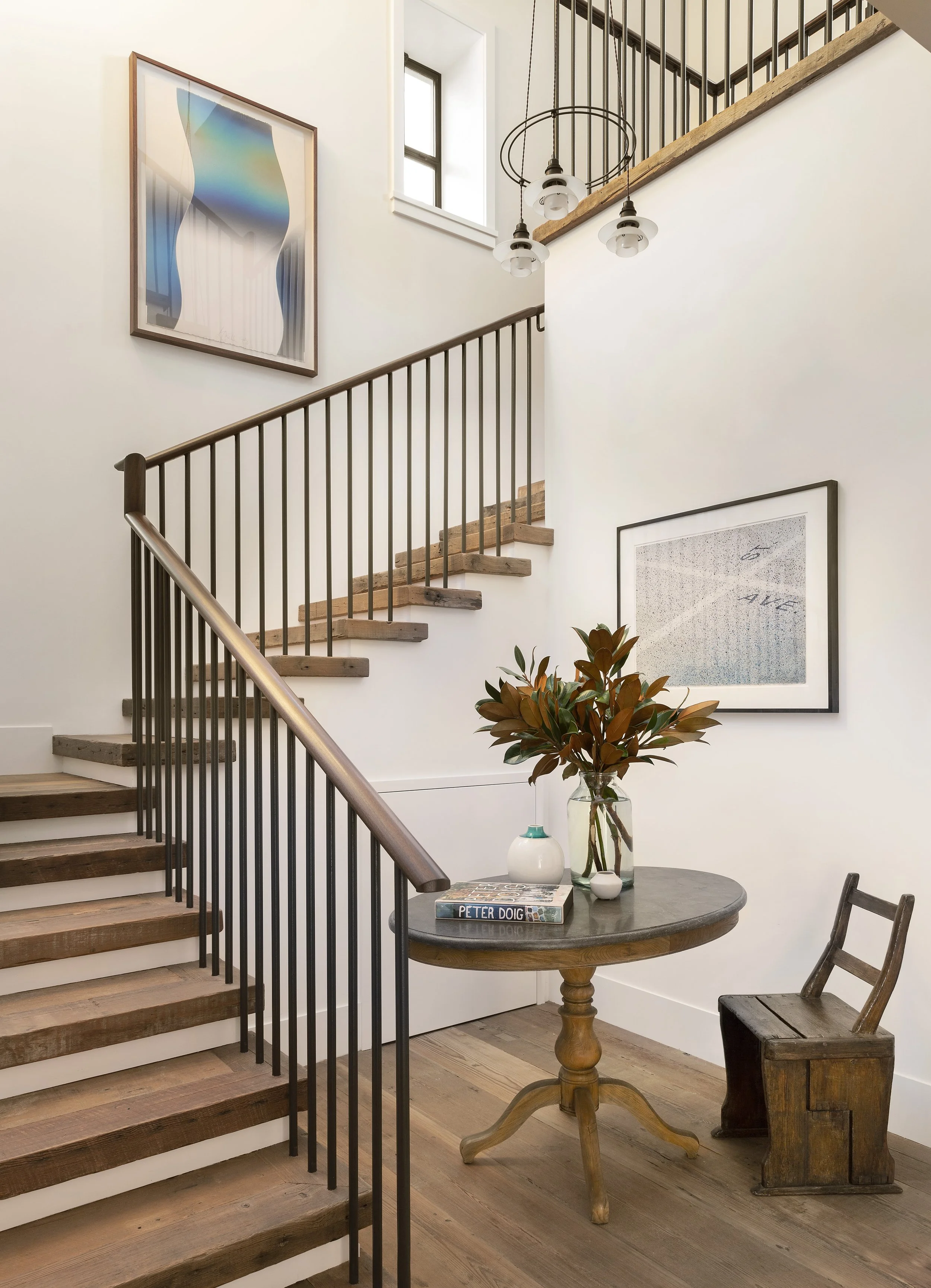 Staircase with black iron balusters and wood treads beside framed art and magnolia branches