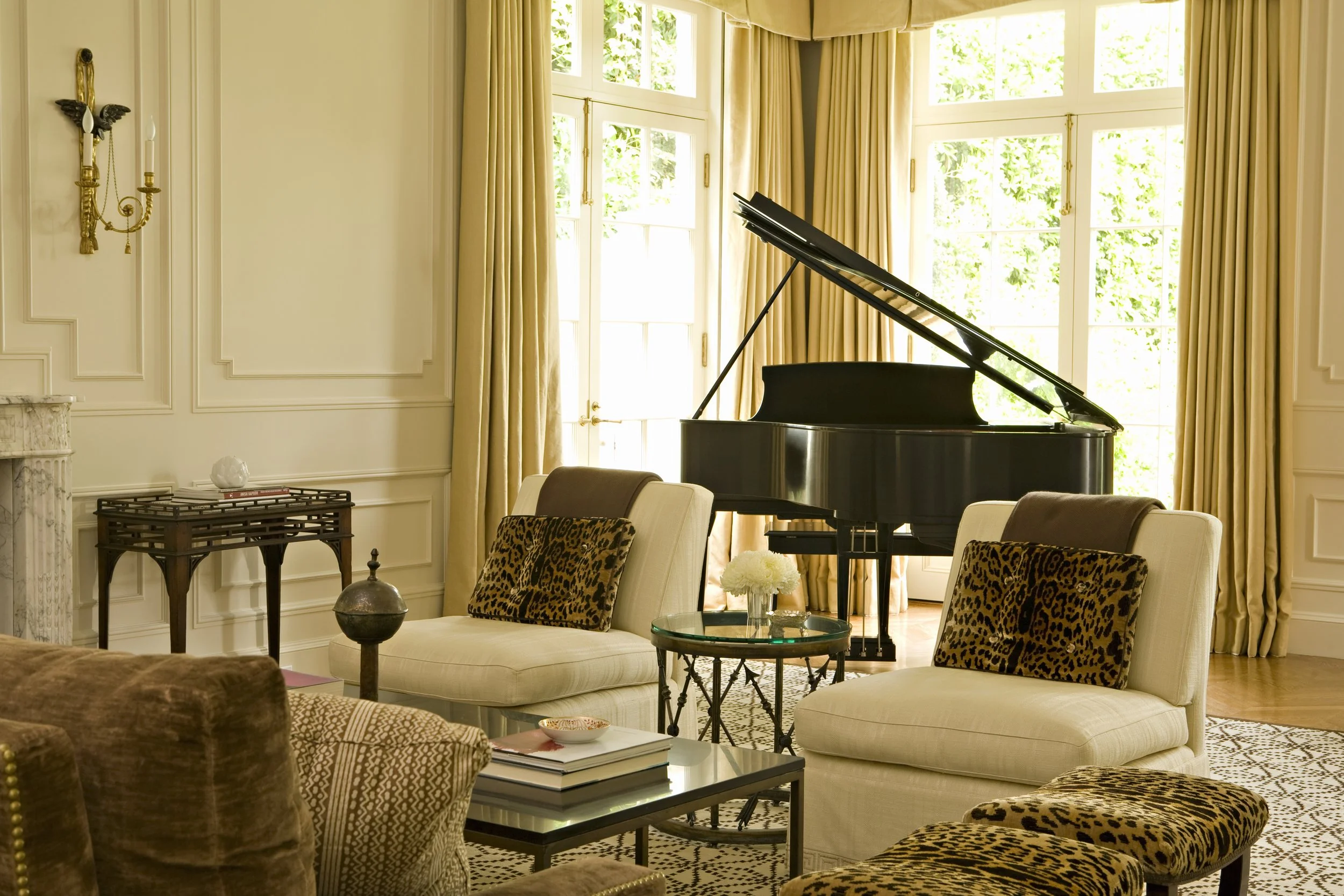 Living room with a grand piano, cream chairs and gold silk drapes