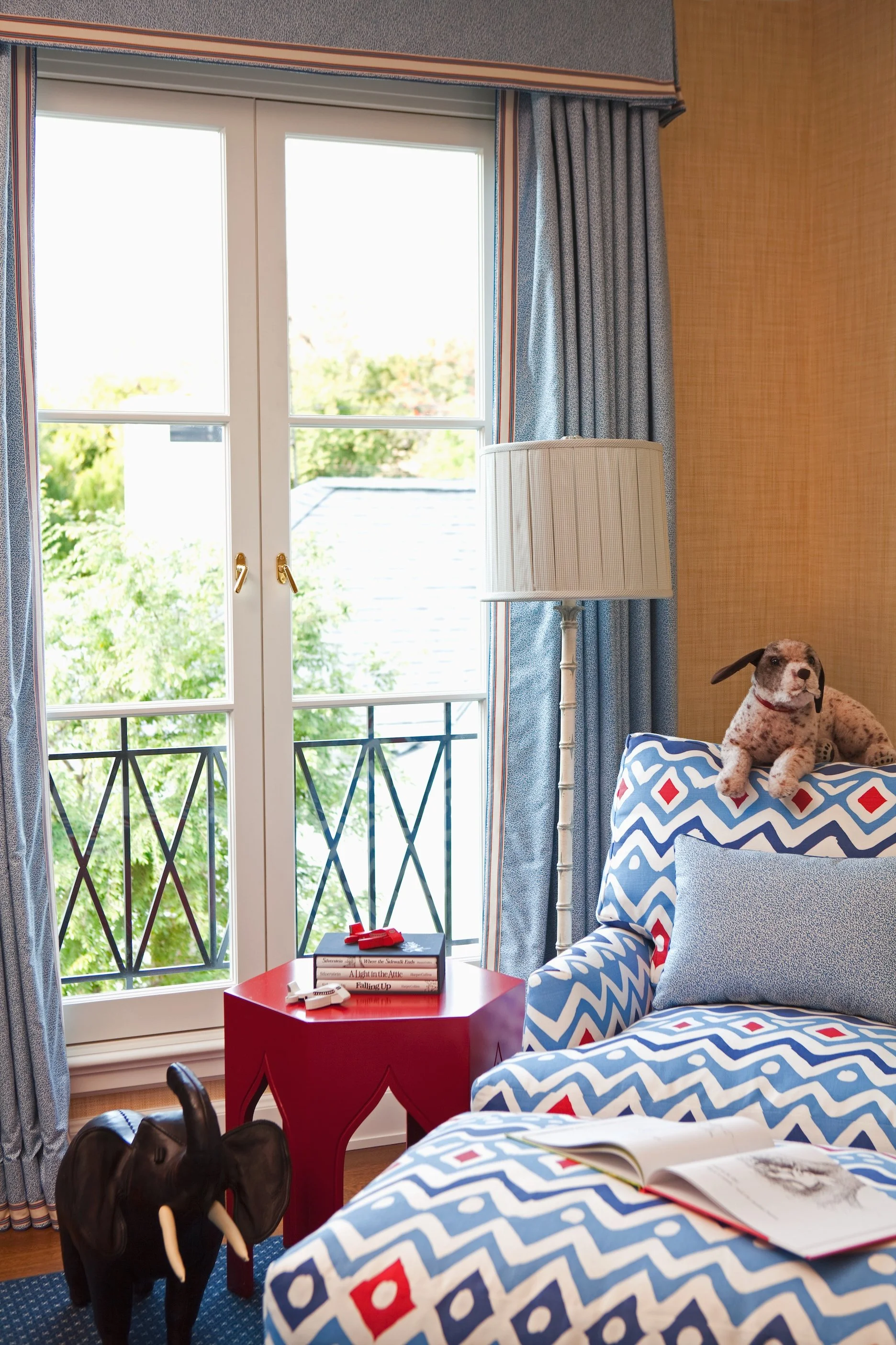 Nursery window with a balcony, a blue and red ikat chair and a stuffed dog