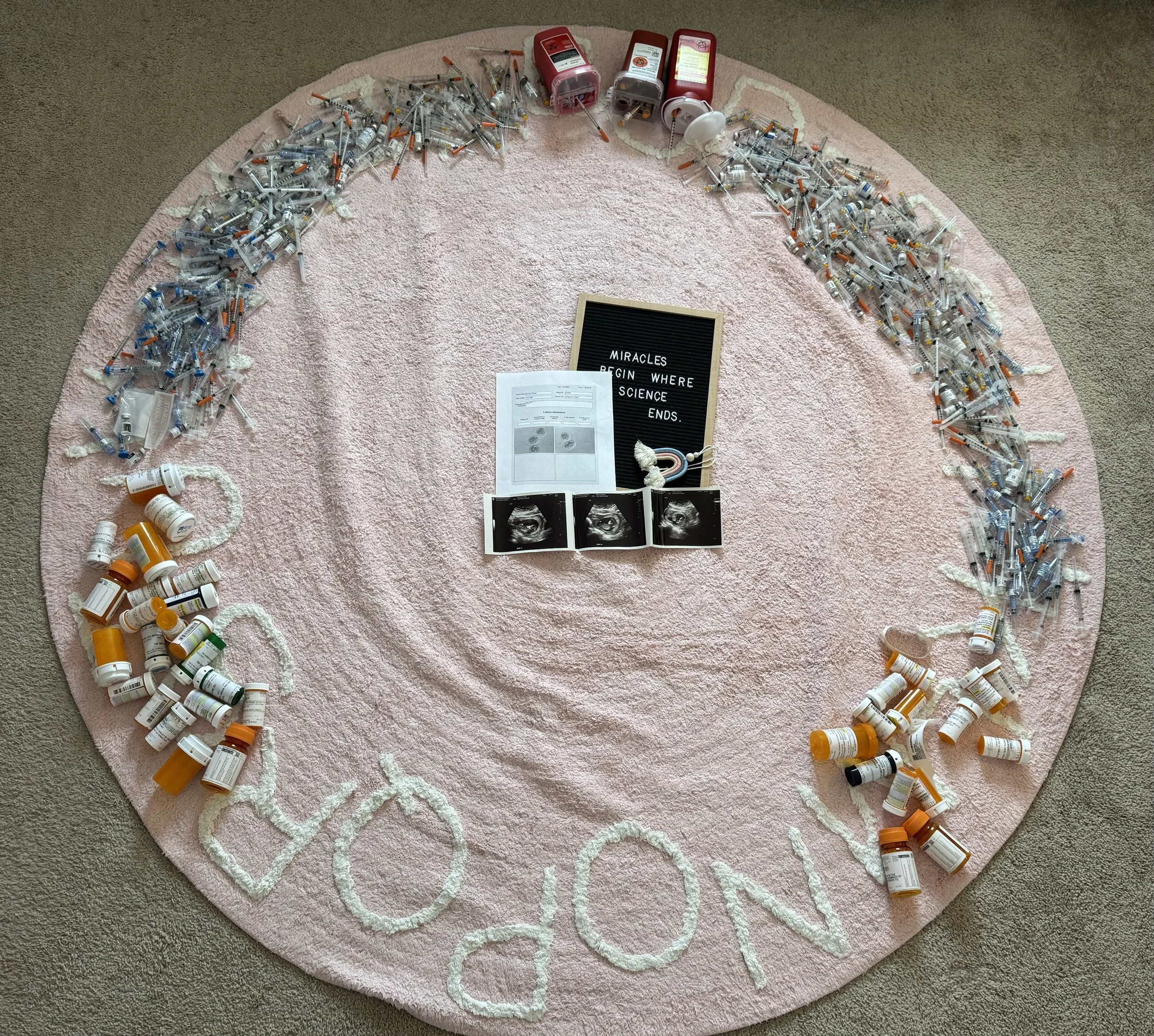 A pink circular rug on carpeted floor, decorated with syringes, pill bottles, and medical supplies, along with a black letter board and ultrasound images.
