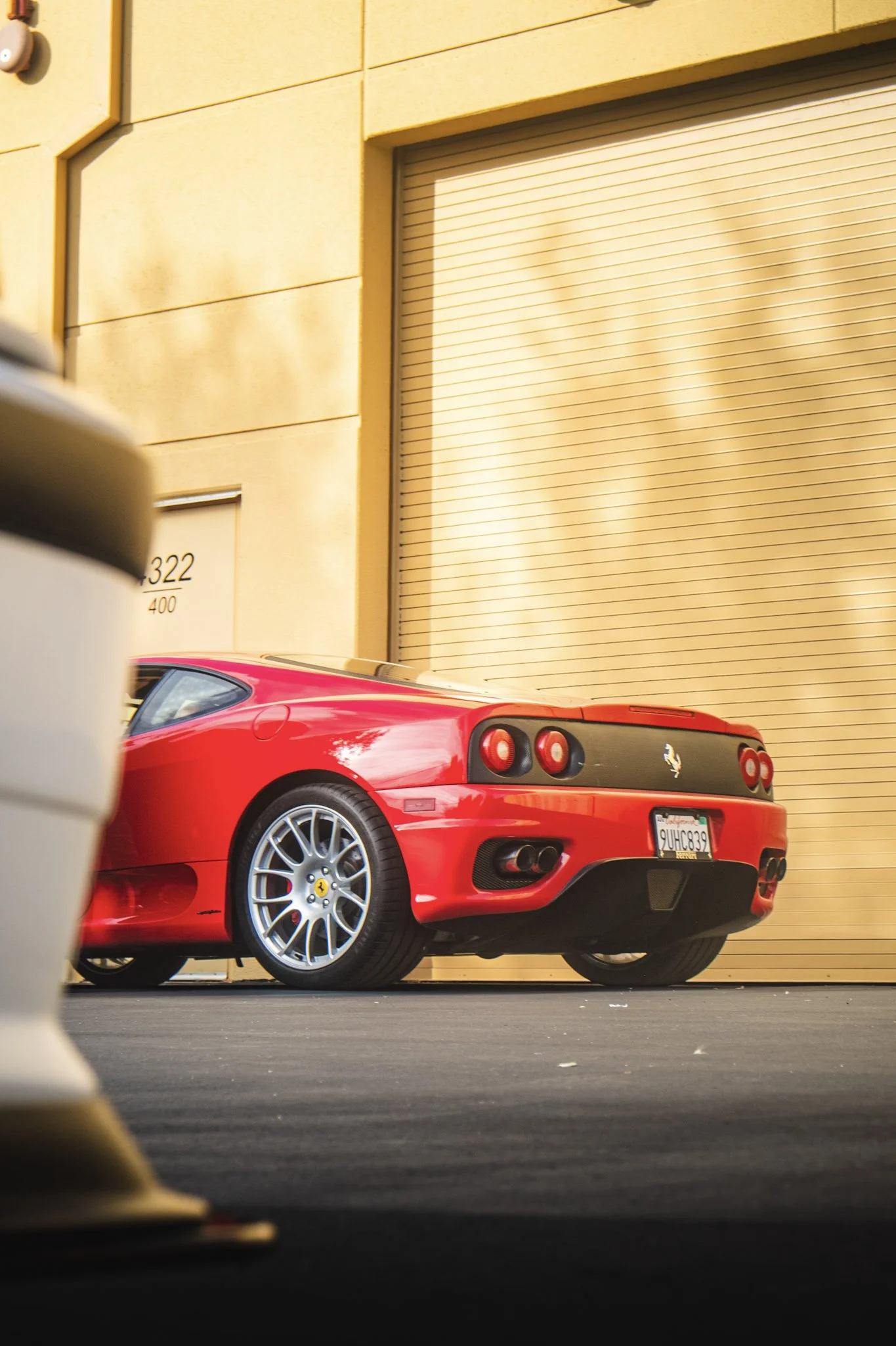 A red Ferrari sports car parked outdoors in front of a beige wall with a closed garage door.