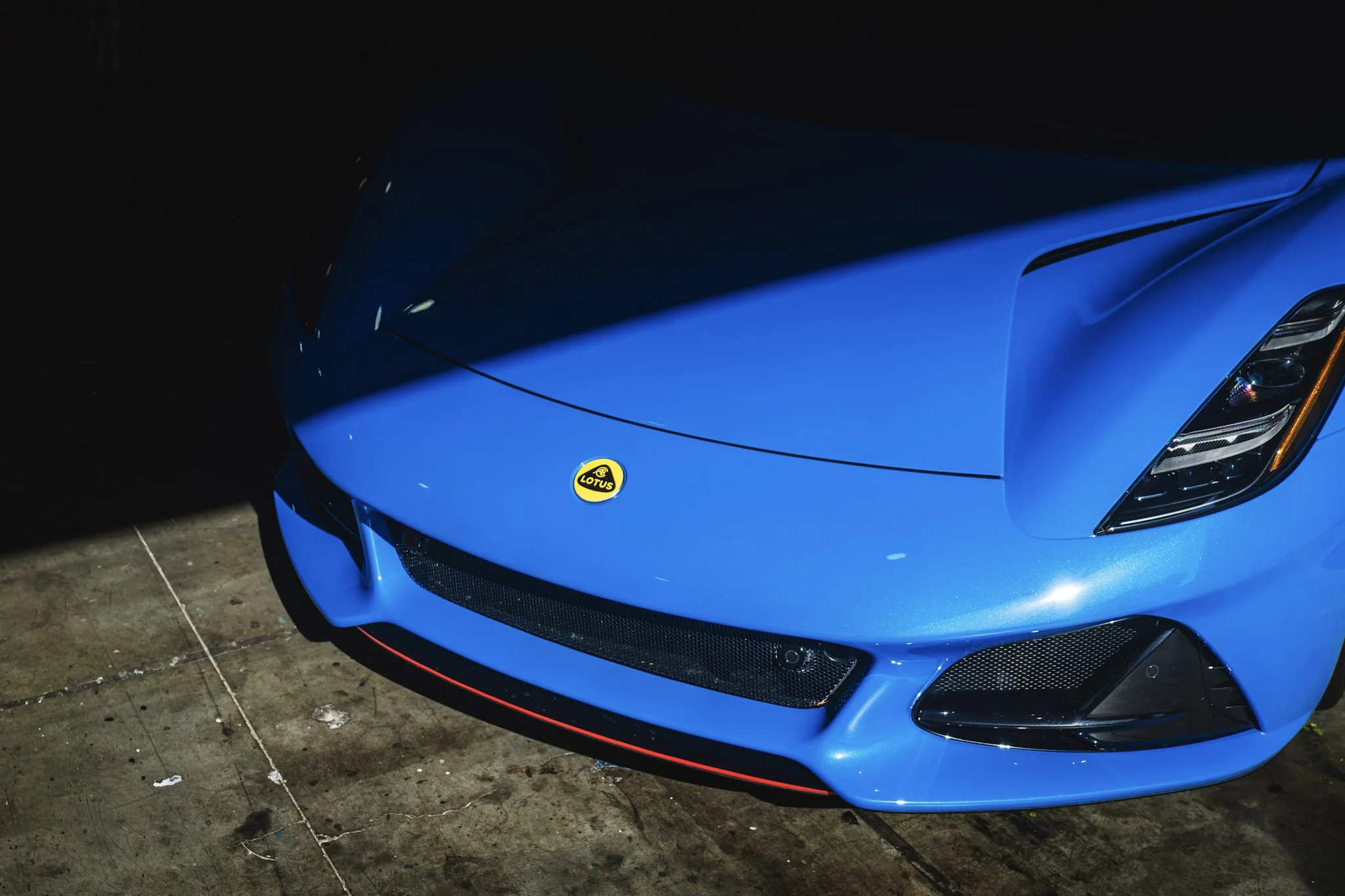 Close-up of a blue sports car with a Lotus emblem, parked on a concrete surface with a dark background.