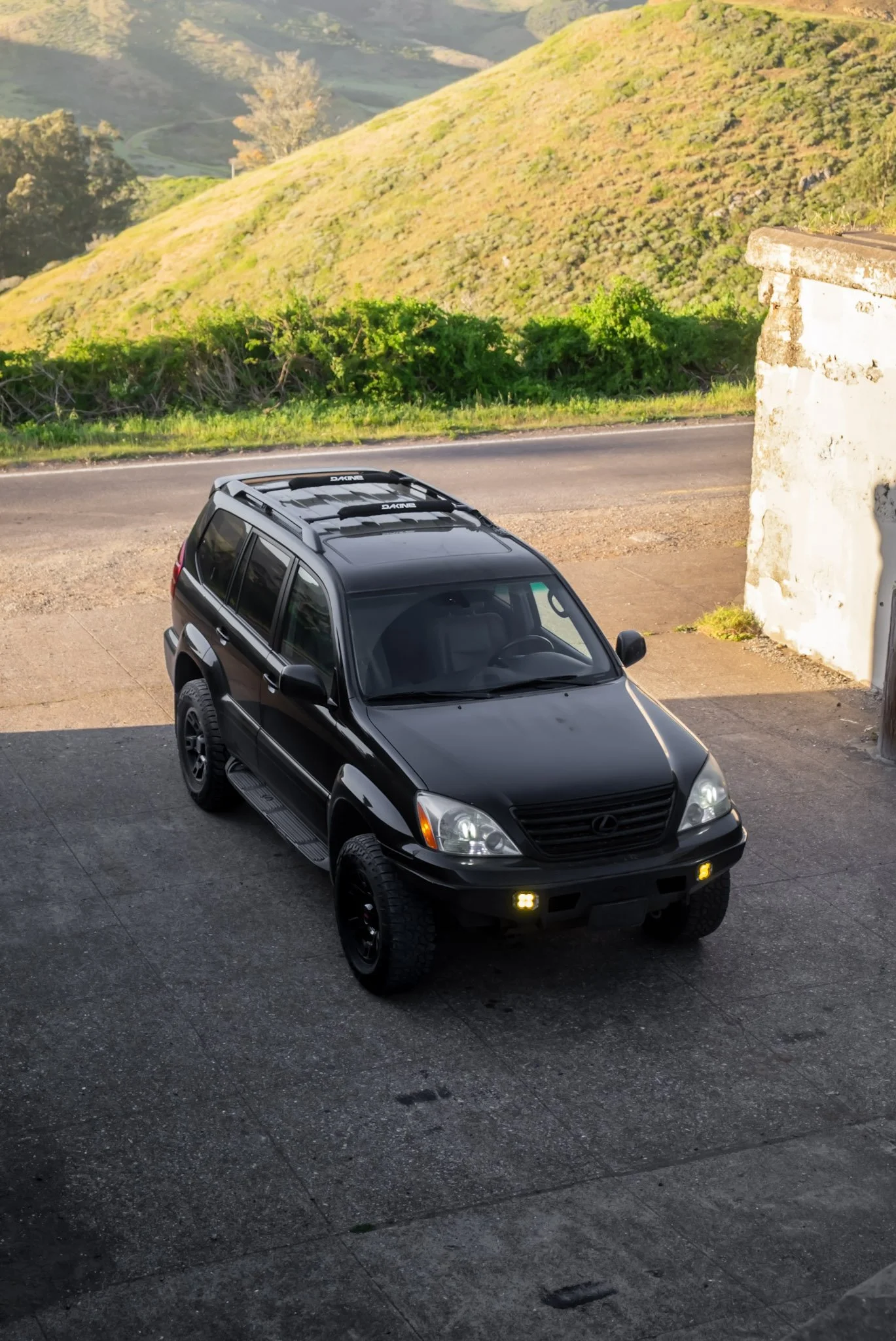 A black Lexus SUV parked on a driveway with hills and a road in the background.