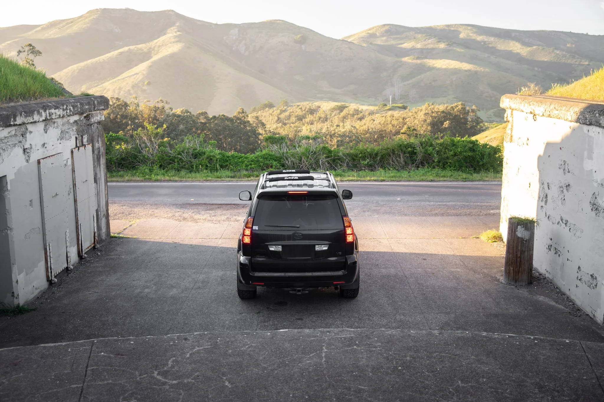 A black SUV parked in a driveway under an overpass with mountains in the background.