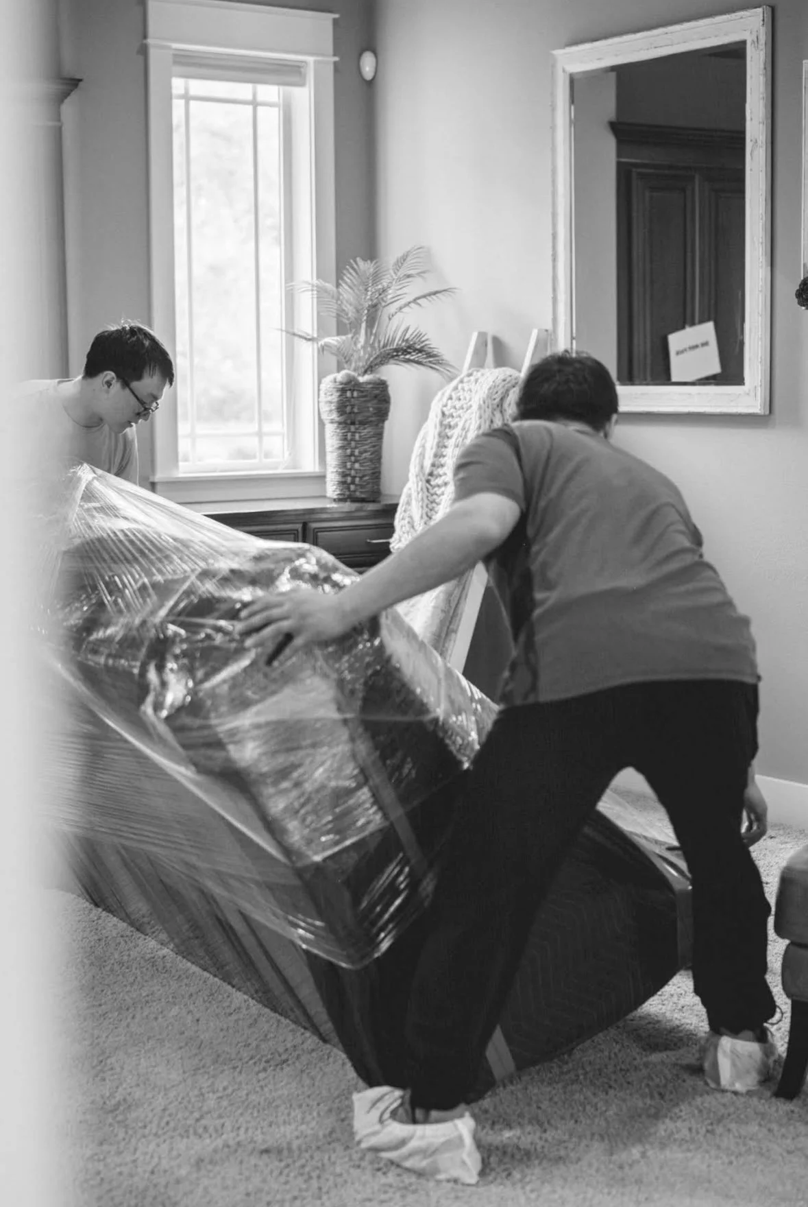 Two movers carefully handling a large wrapped furniture item inside a home.
