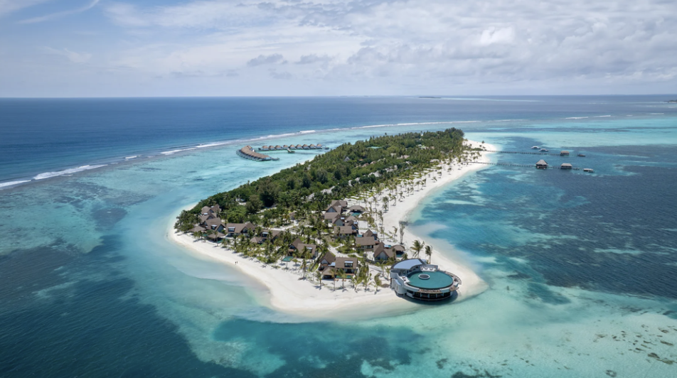 Aerial view of a tropical island resort surrounded by turquoise coral reefs and ocean.