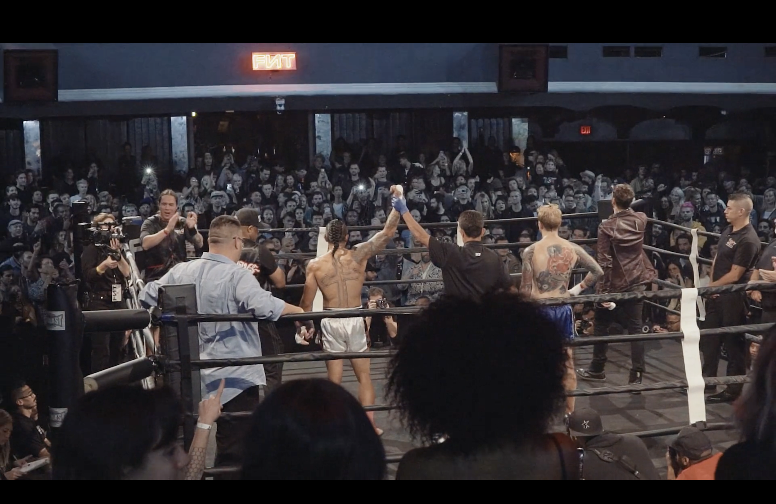 Crowded boxing ring with fighters and crew celebrating as a large audience watches and takes photos.