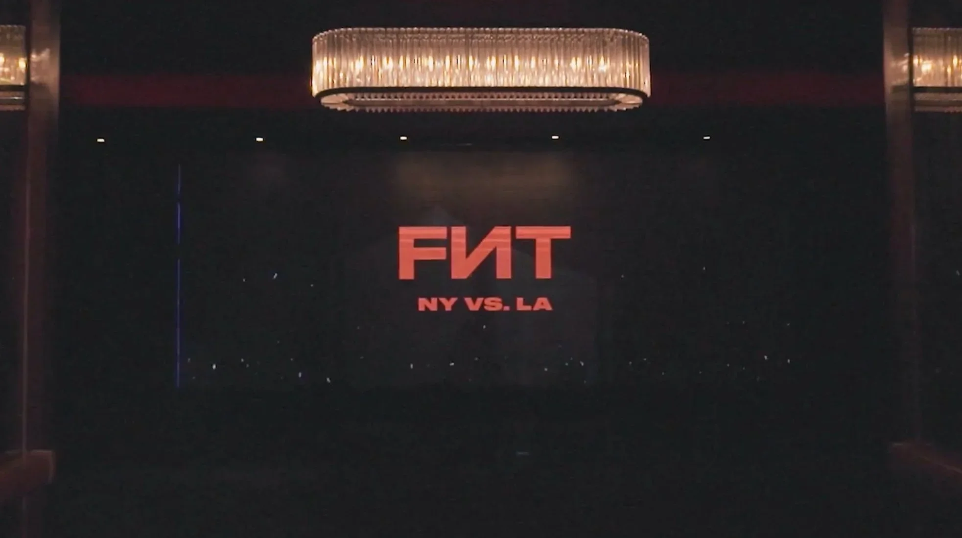 Dark theater marquee displaying red “FNT” and “NY VS. LA” beneath a chandelier