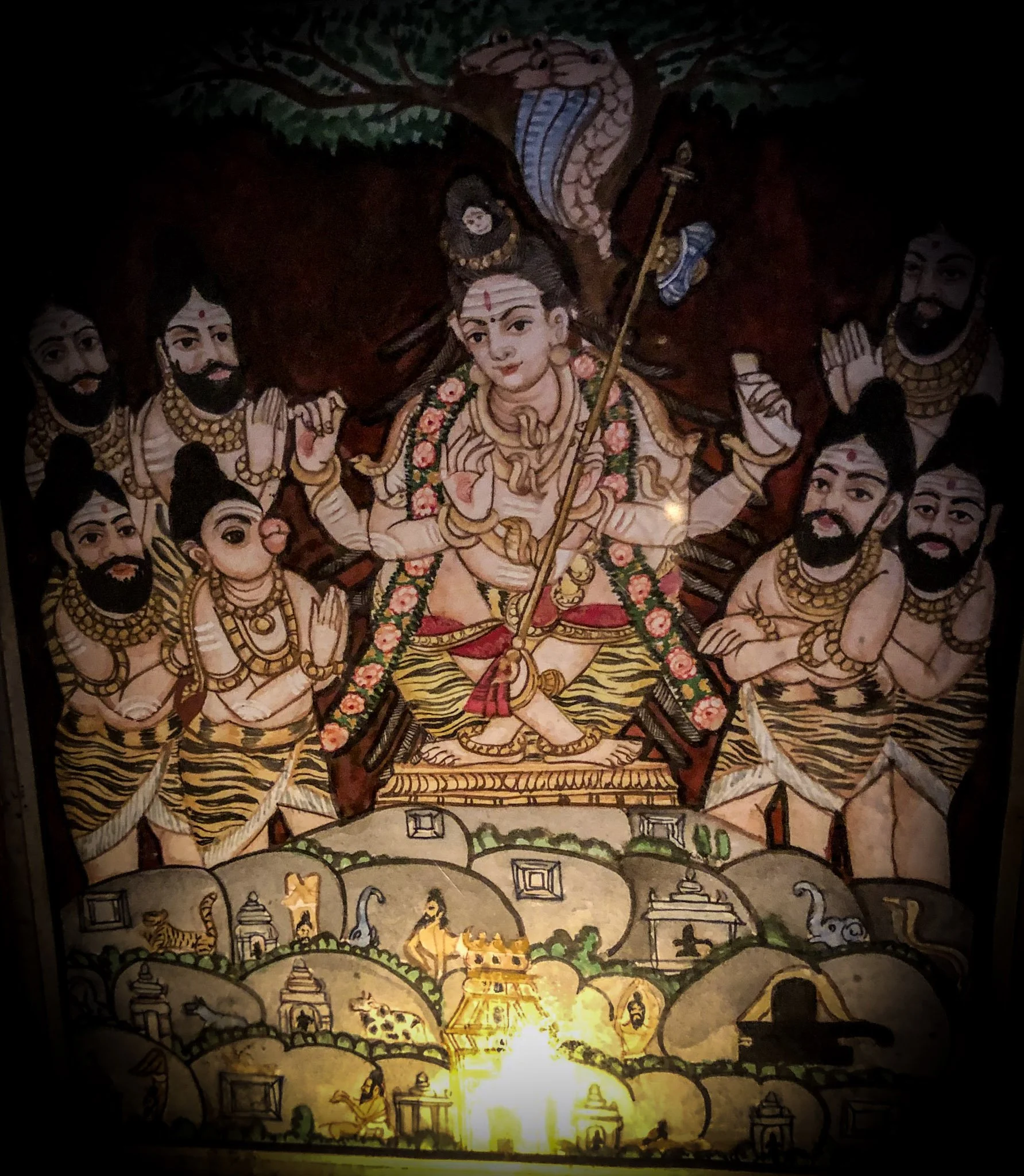 Hindu religious art depicts a multi-armed goddess in the center surrounded by four male deities, with multiple tiers of small sculptures and illustrations below, illuminated from below.