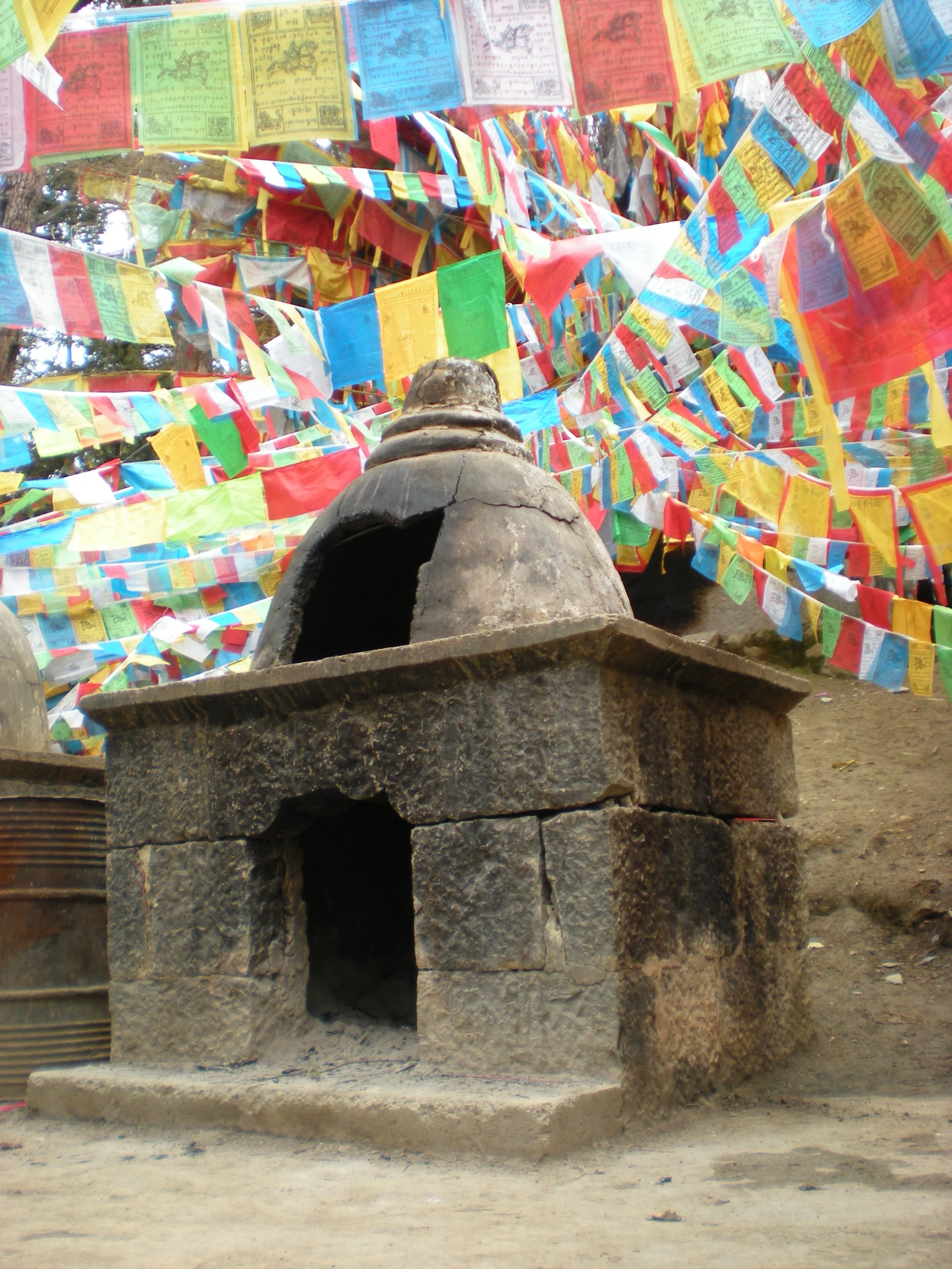 Ancient stone stupa in front of colorful prayer flags flying in the wind.
