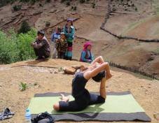 Person doing a stretch yoga pose on a mat outdoors, with people and a canyon in the background.