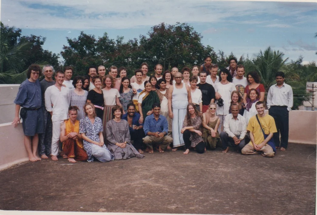 A large group of diverse people gathered outdoors on a rooftop with trees and a partly cloudy sky in the background, posing for a photo.