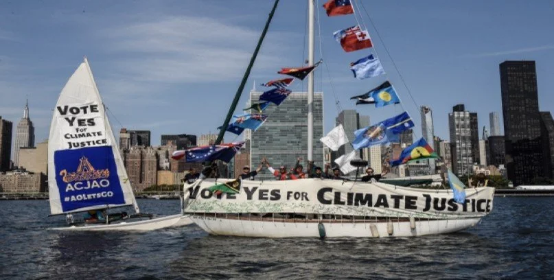 Sailing boats flying Pacific Island flags and 'Vote Yes for Climate Justice' banners in front of UN Headquarters, New York
