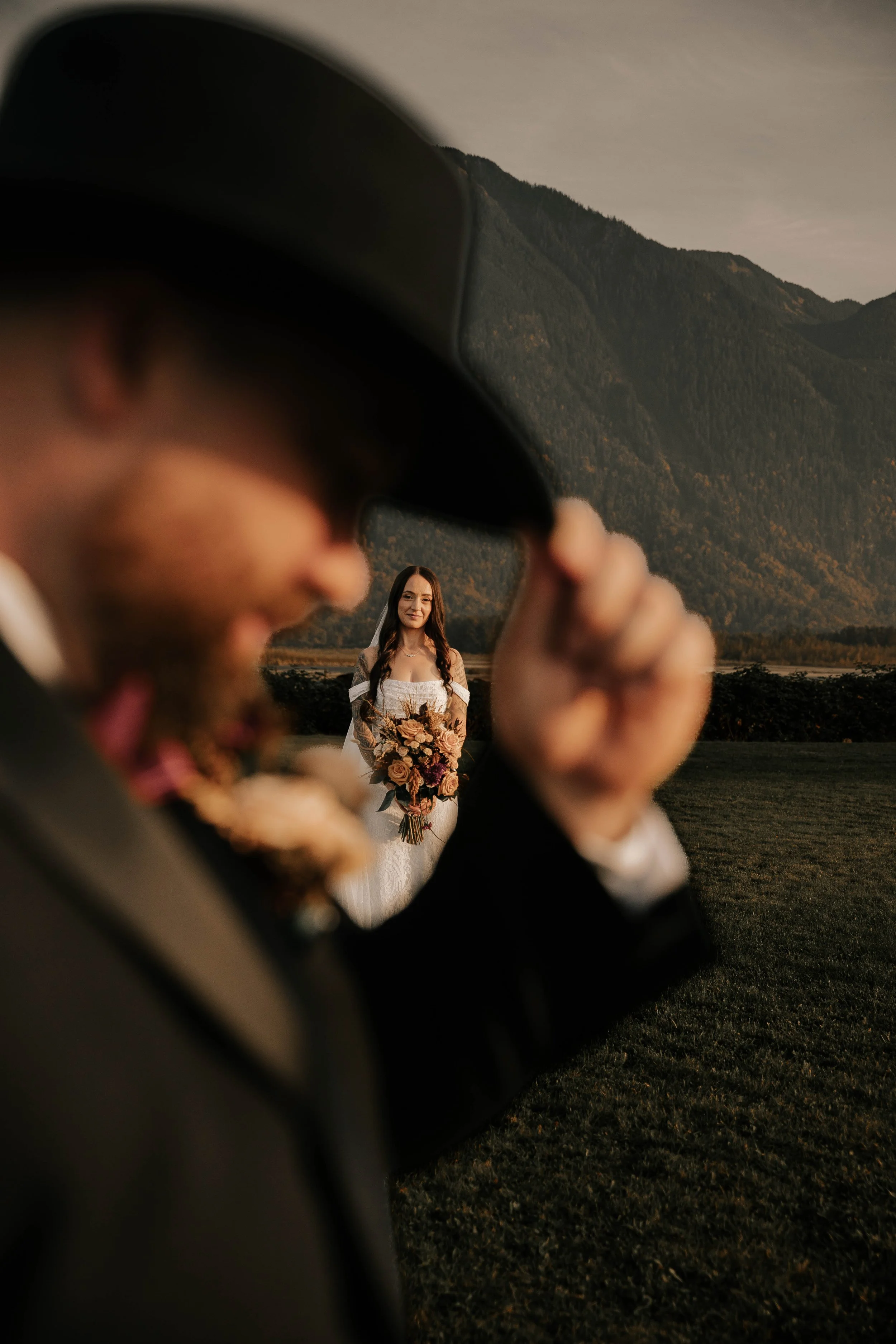 Fraser River Lodge mountain side wedding. Rustic country warmth in the golden hour light. Vancouver Bride and Groom. An artistic shot of bride through the groom's cowboy hat