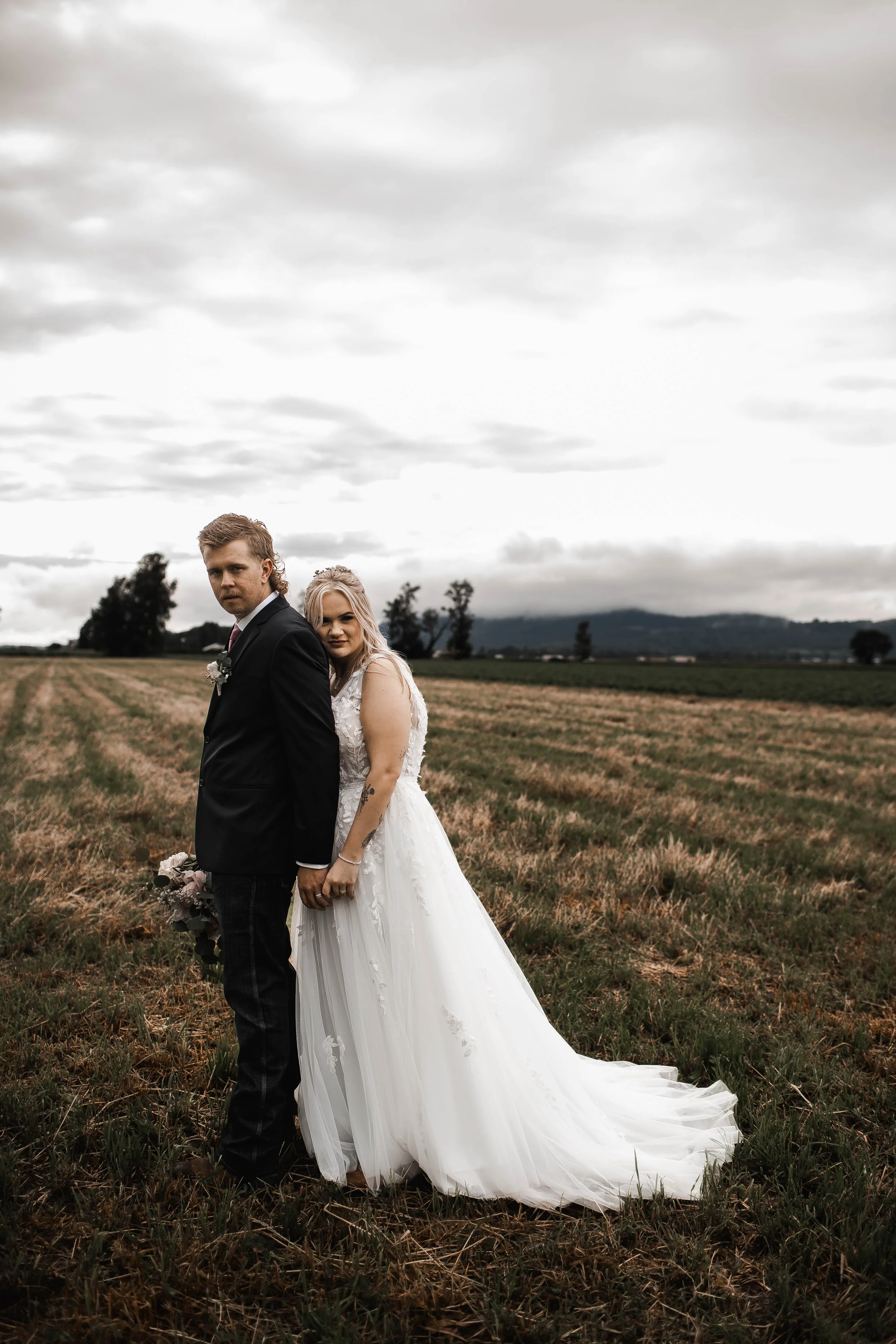 Newlyweds posing together in an open countryside field beneath a cloudy sky. in Langley