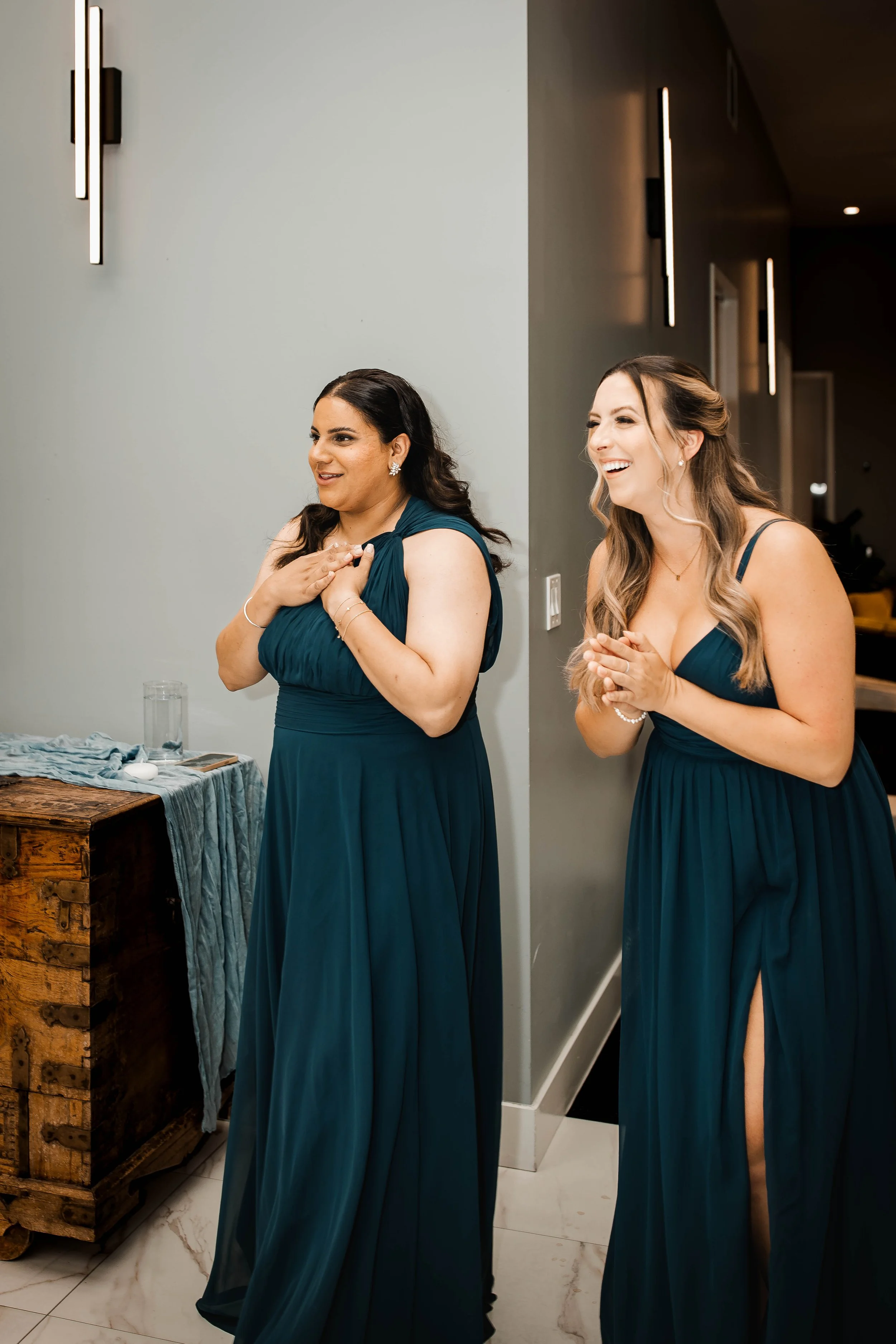Bridesmaids in dark teal dresses sharing an emotional moment during wedding preparations.