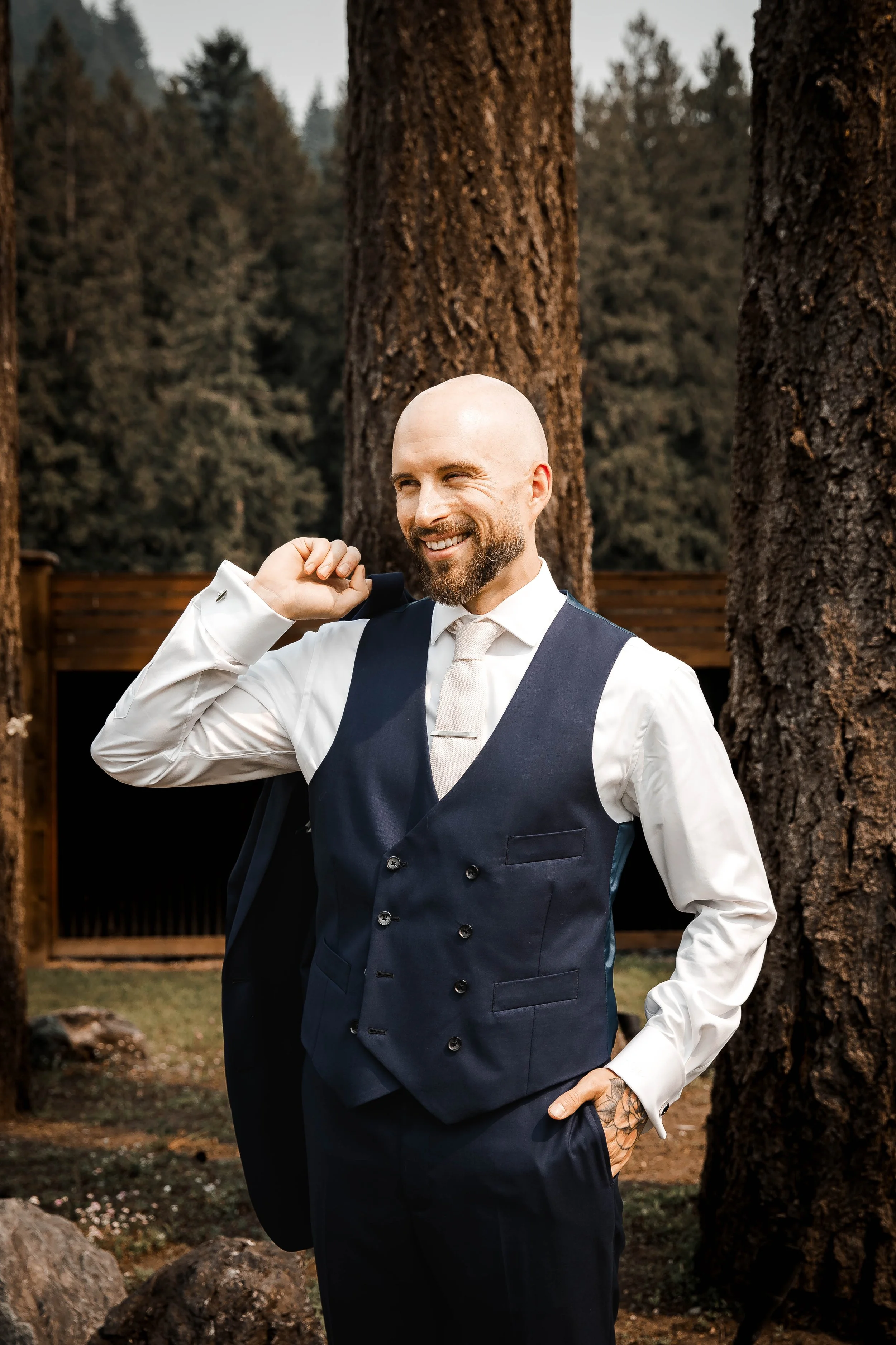 Groom smiling while adjusting his wedding attire during outdoor portraits.