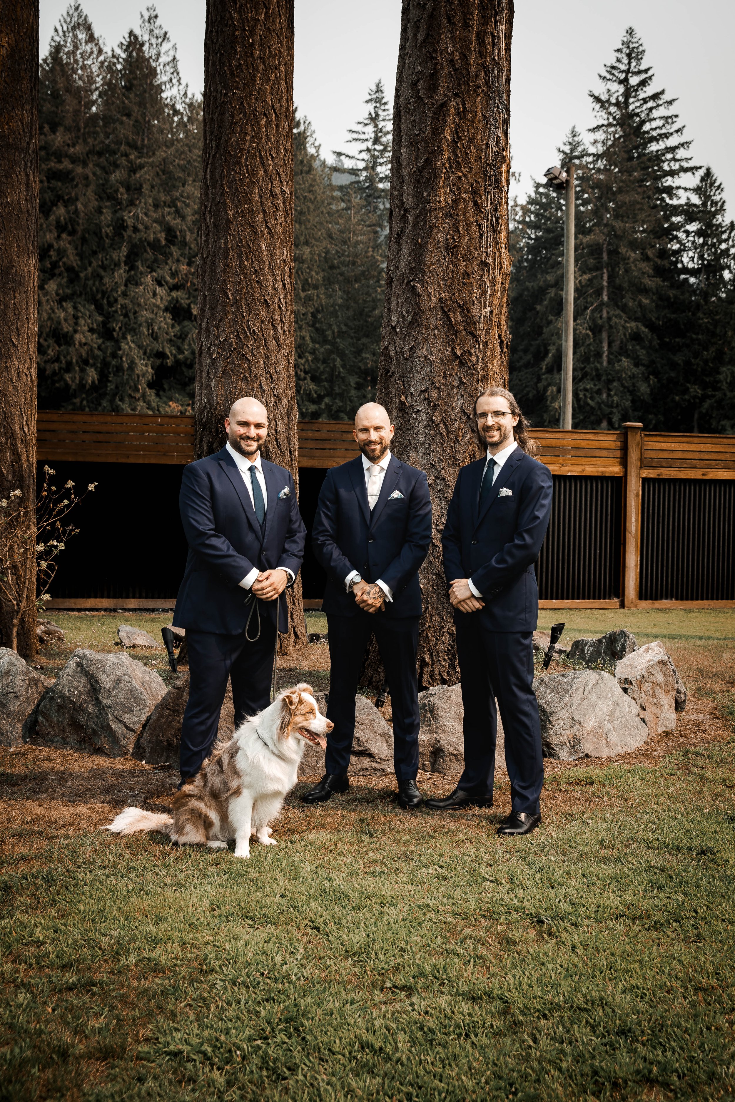 Groom and groomsmen posing outdoors with a dog among the trees at Bridlewoods in Chilliwack.