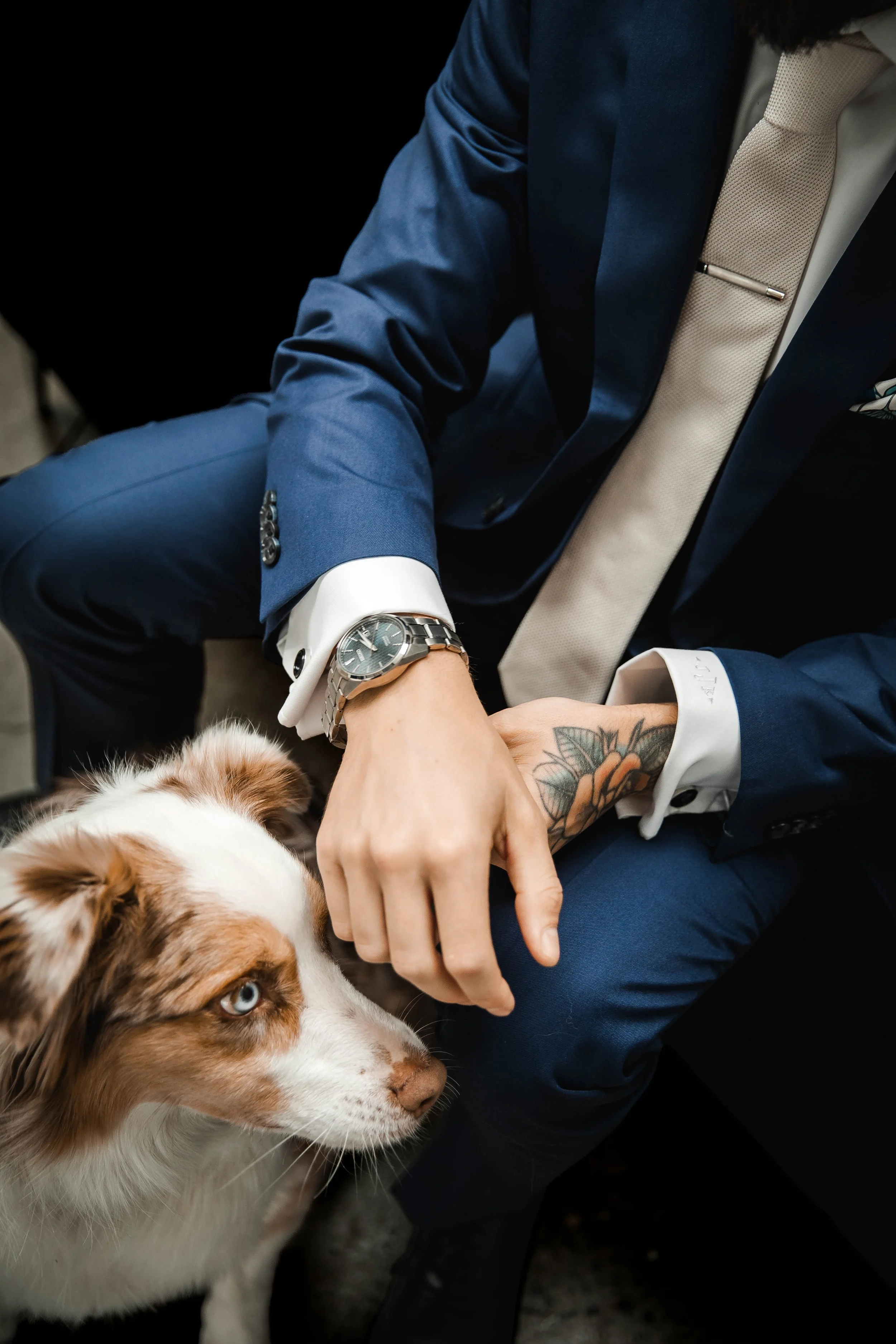 Close-up of groom in a navy suit petting a dog during wedding celebrations.