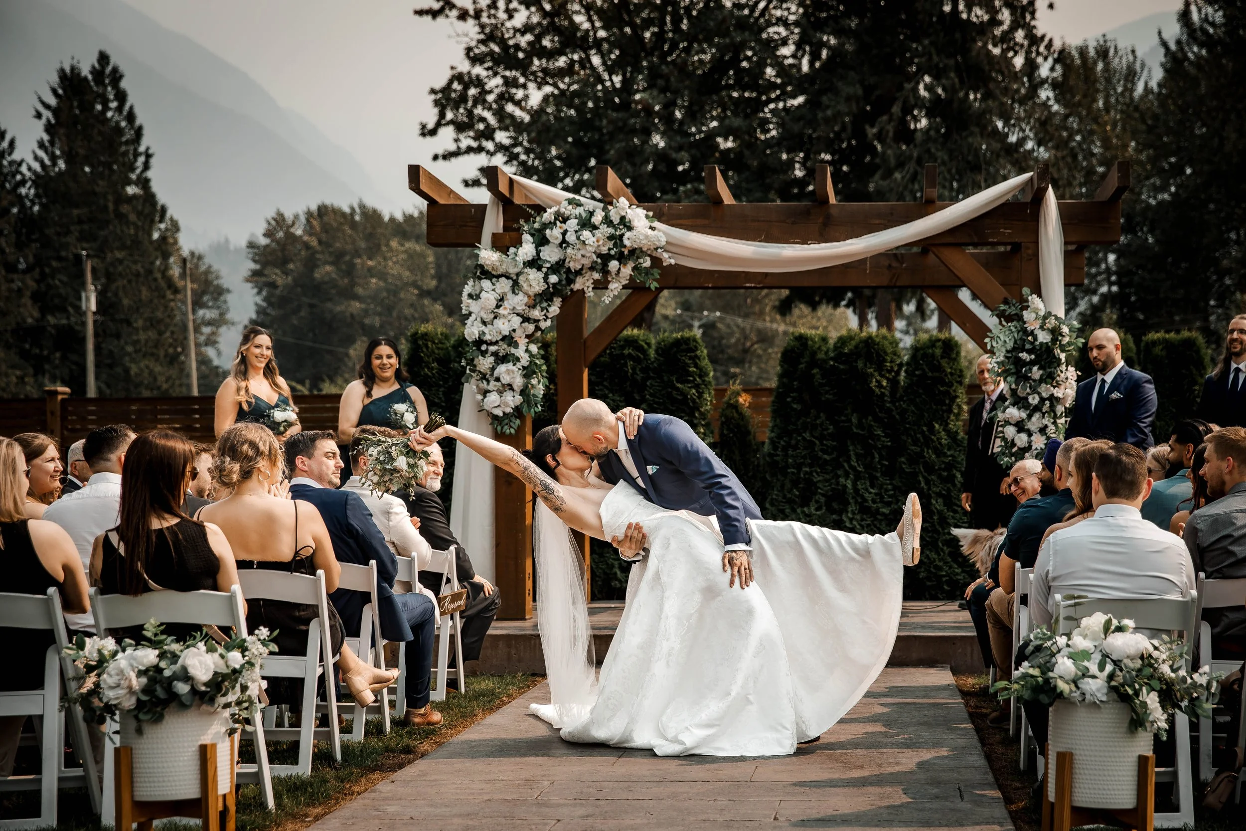Groom dipping his bride for a romantic kiss beneath the wedding ceremony arch.
