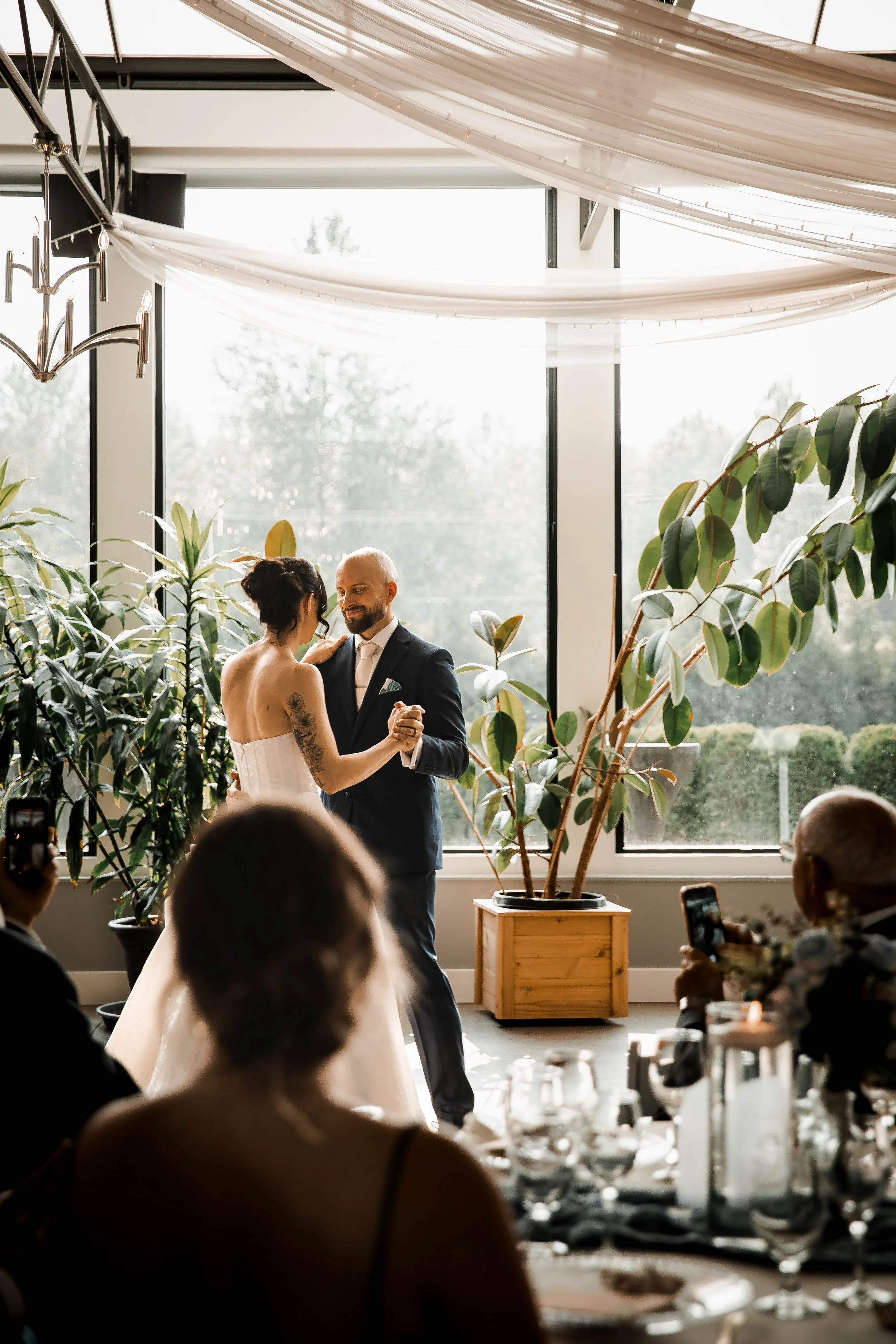 Bride and groom sharing their first dance surrounded by greenery and natural light.