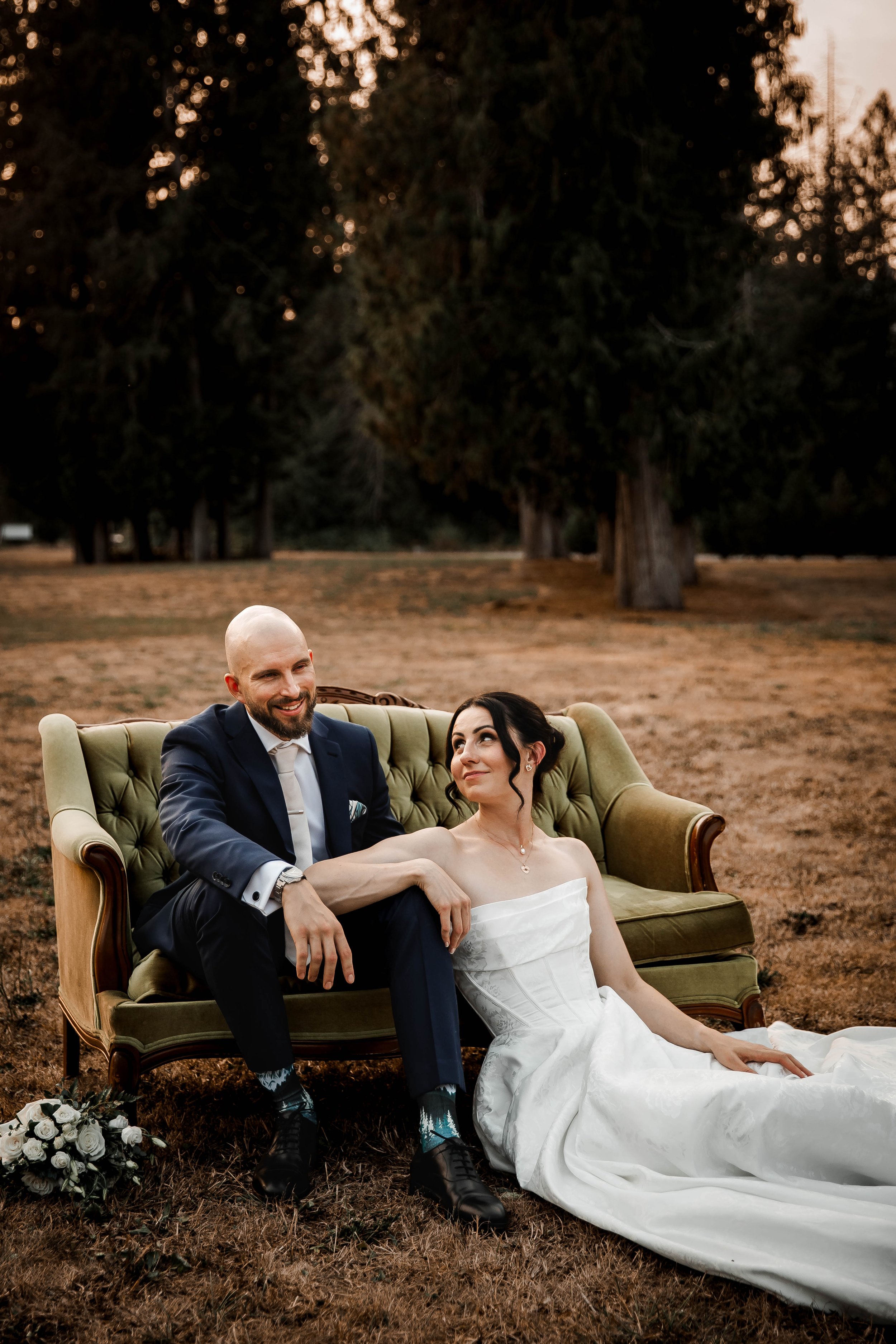 Newlyweds relaxing together on a vintage-style sofa during their wedding portraits.