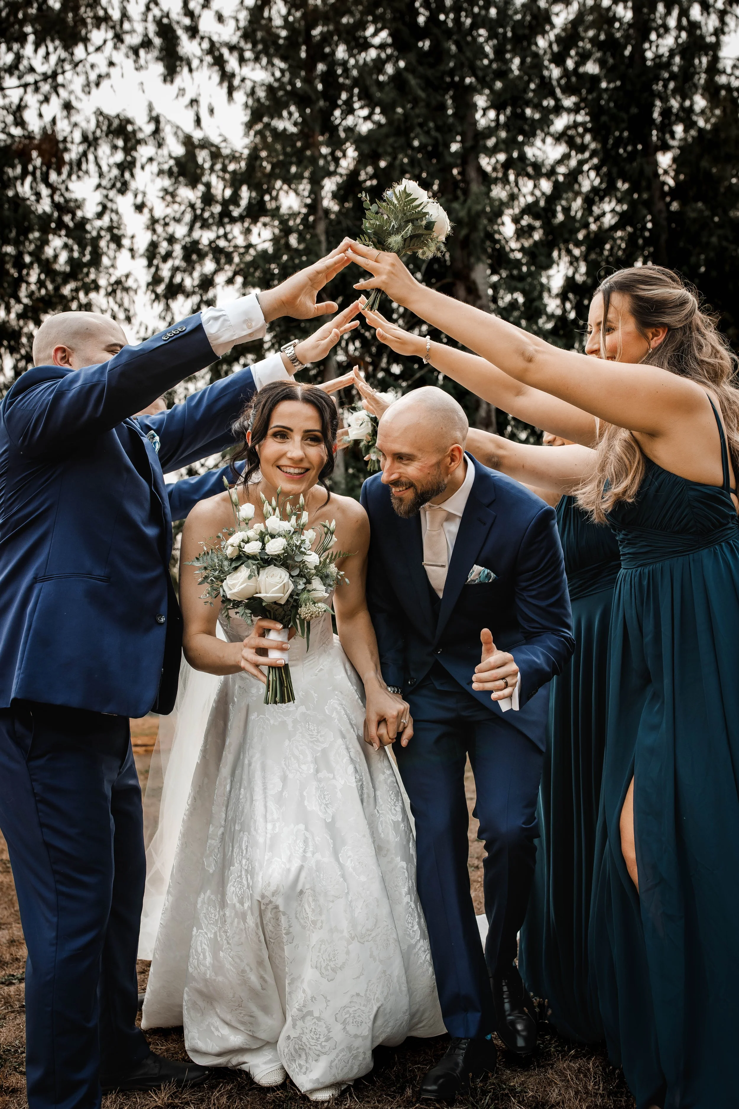 Bride and groom laughing as their wedding party raises bouquets overhead.