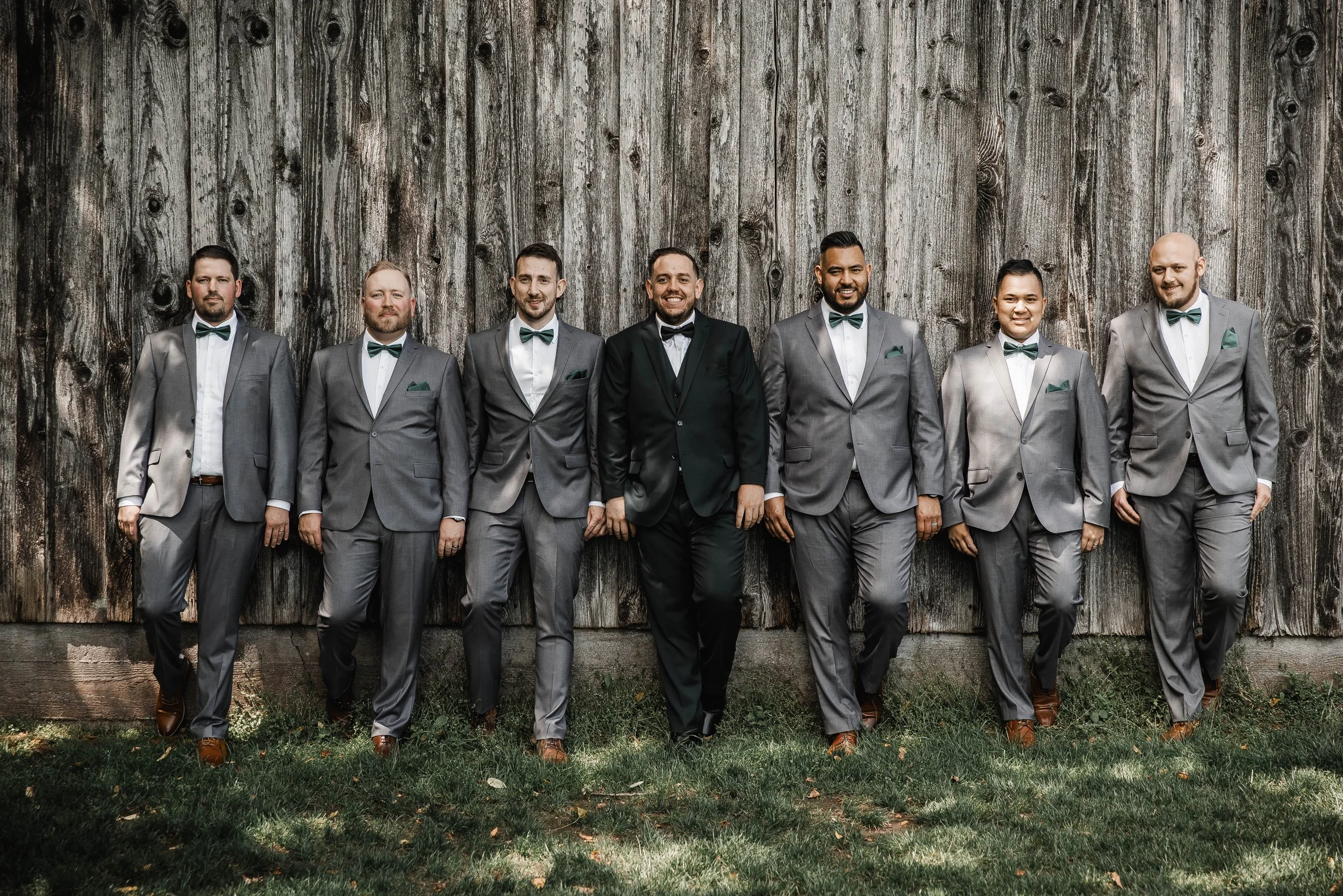 Groom and groomsmen posing in formal suits against a weathered barn wall during an Estate 248 wedding in Aldergrove.