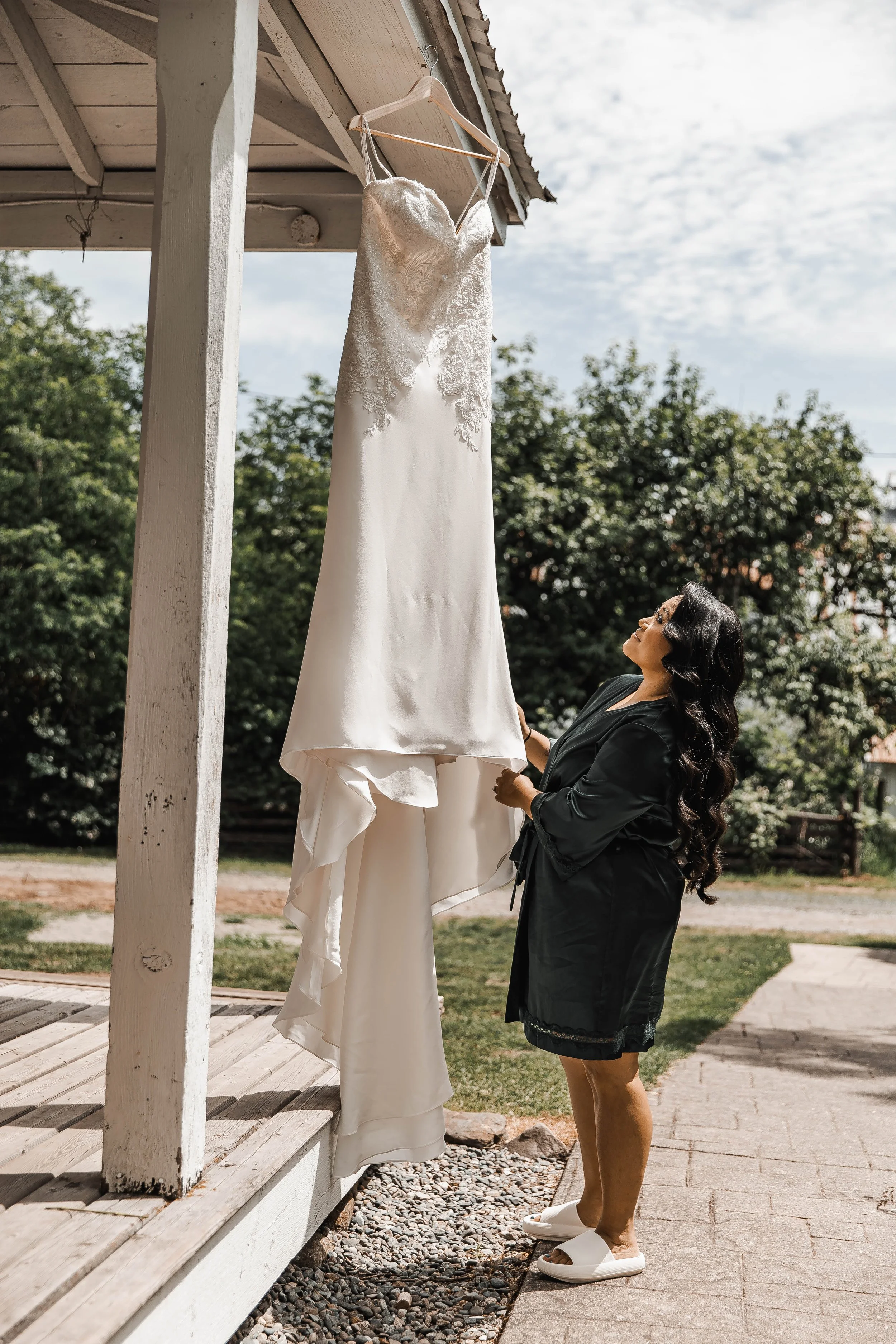 Bride admiring her wedding dress hanging outdoors beneath a rustic wooden porch at Estate 248 wedding venue.