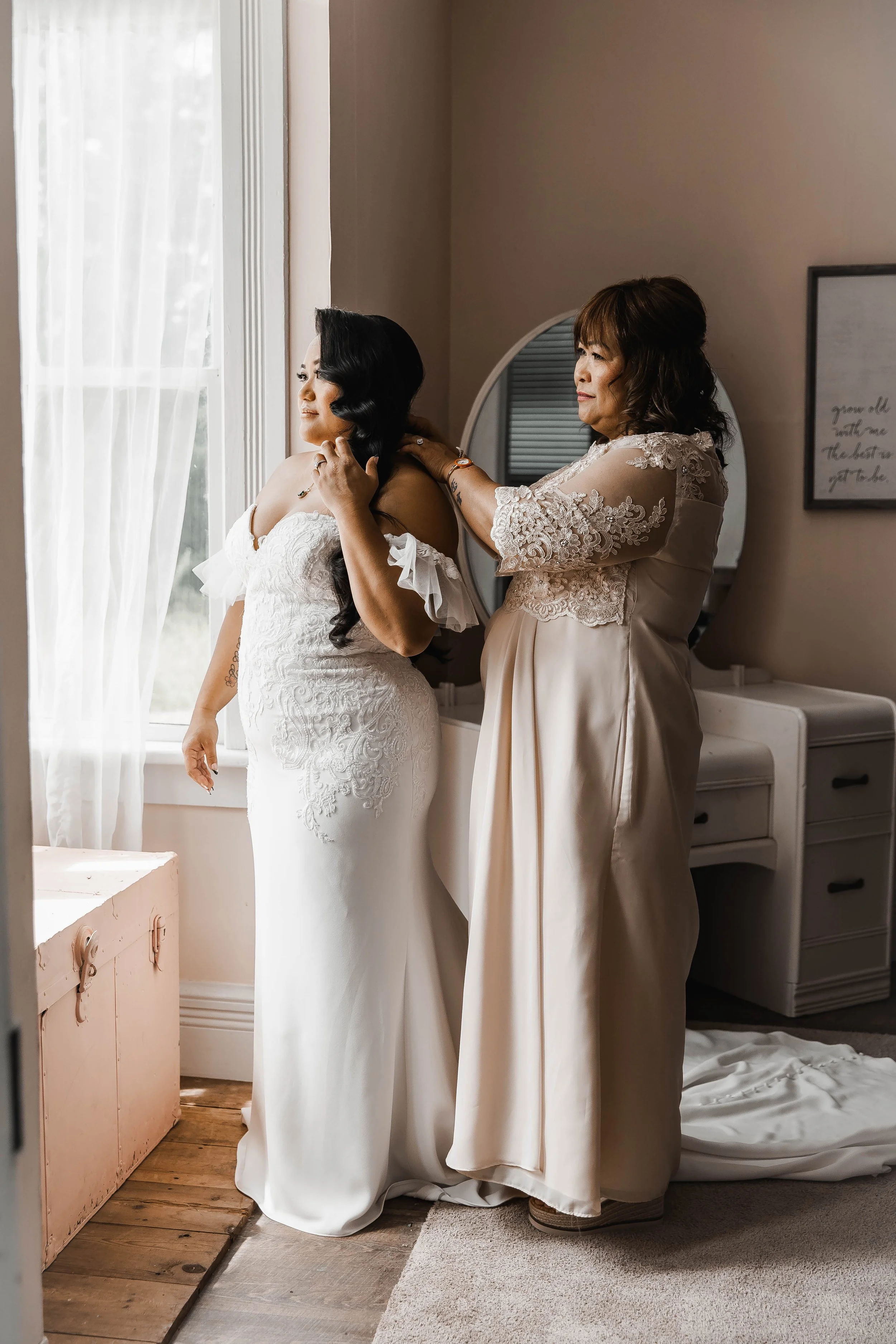 Bride getting ready with help from a loved one beside a softly lit window before her Estate 248 wedding ceremony.