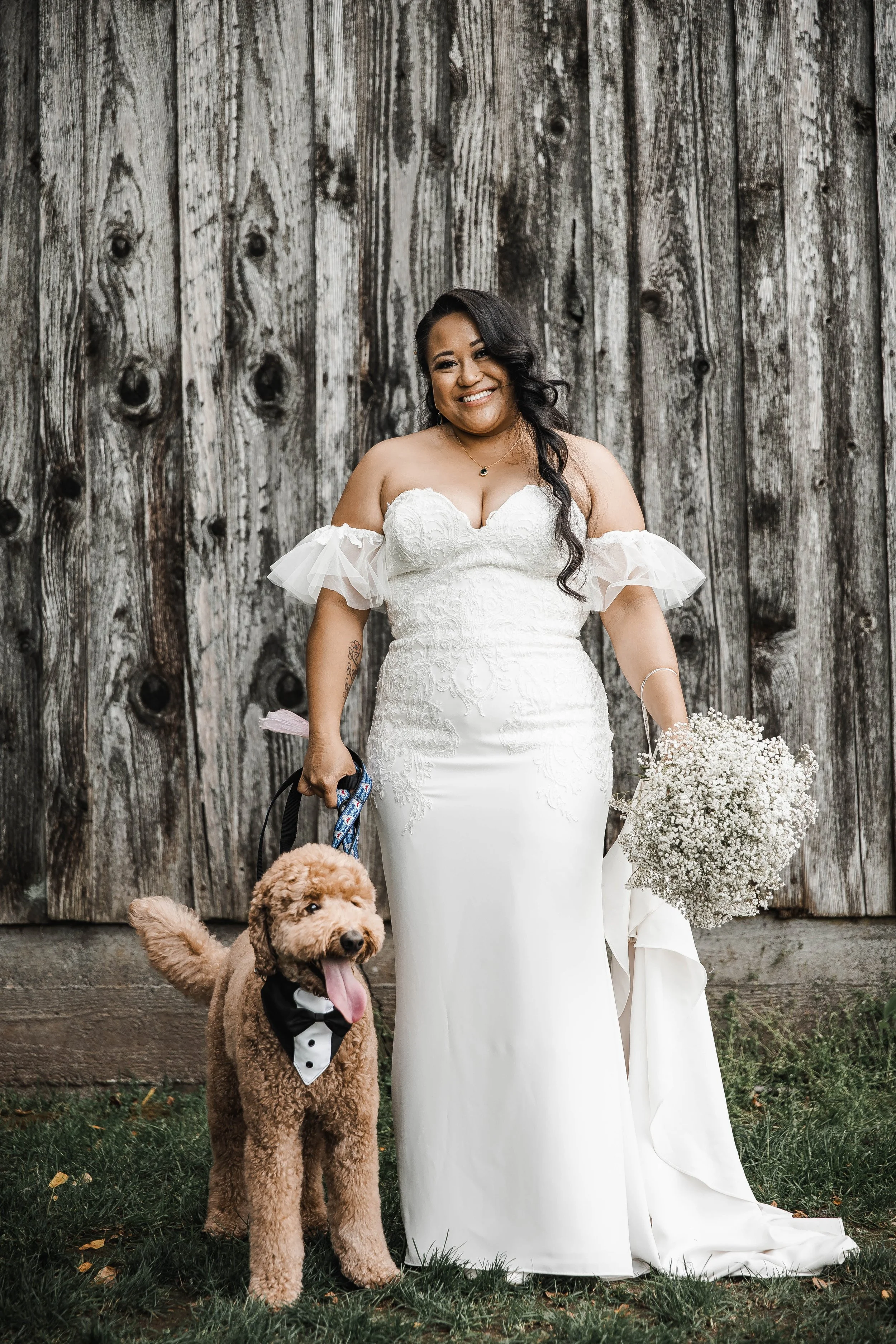 Bride posing with her dog in front of a weathered wooden barn during her rustic Estate 248 wedding celebration.
