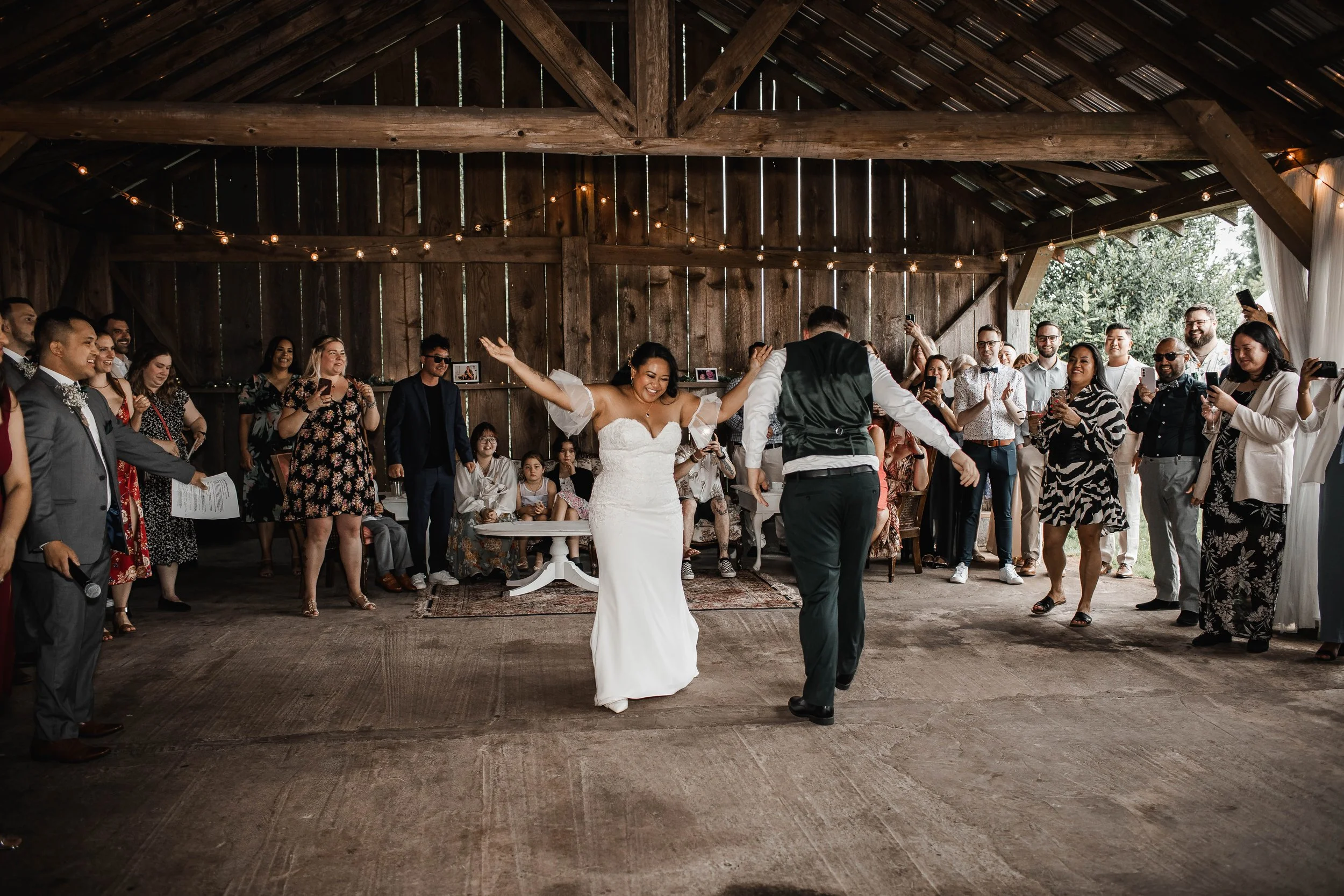 Bride and groom dancing beneath warm string lights inside the rustic barn at Estate 248 during their wedding reception.