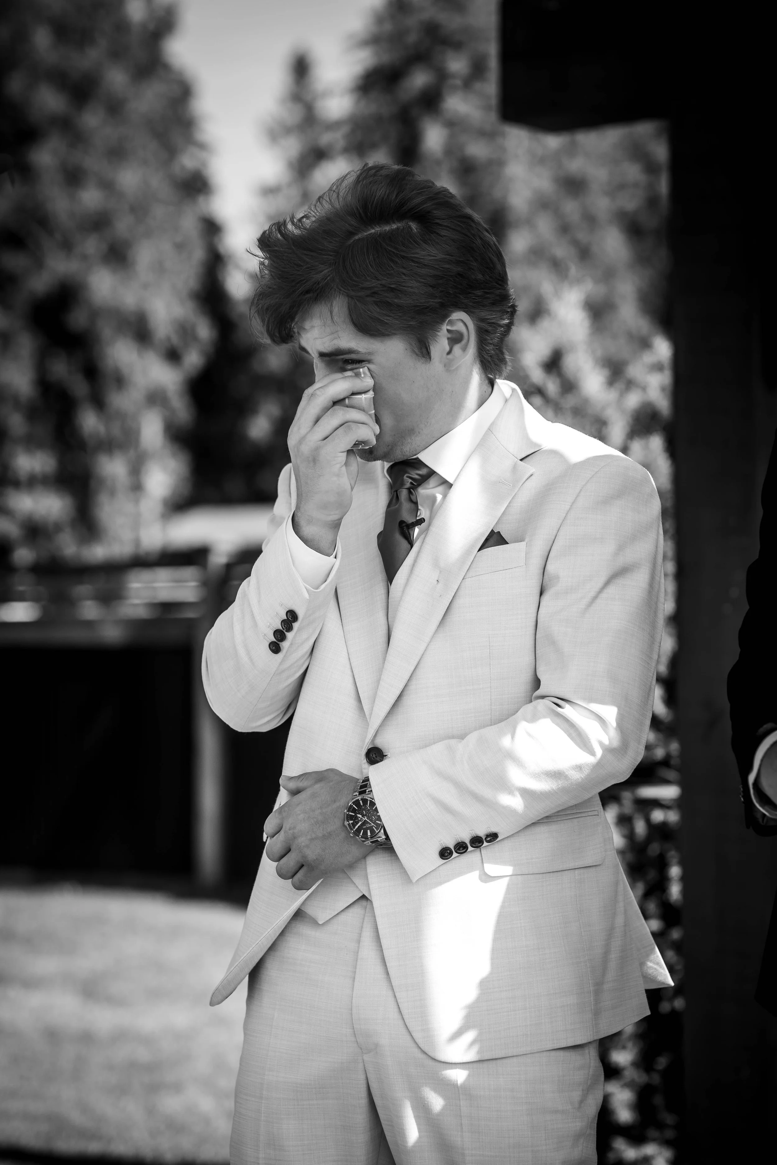 Black-and-white wedding photograph of an emotional groom wiping away tears during his outdoor Bridlewoods ceremony.