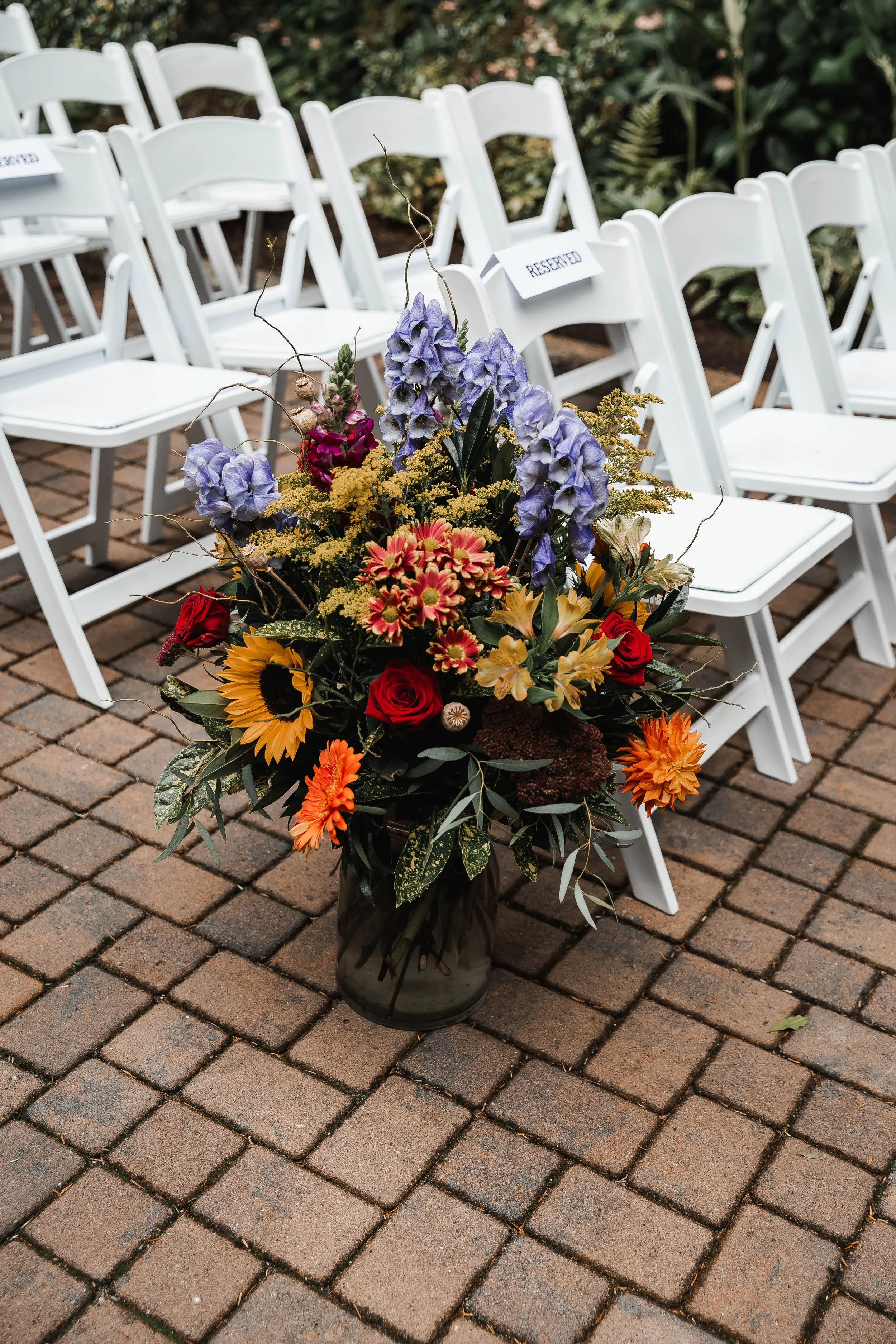 Colourful autumn wedding floral arrangement featuring sunflowers, red roses, orange blooms and purple flowers at Whonnock Lake in Maple Ridge, BC.