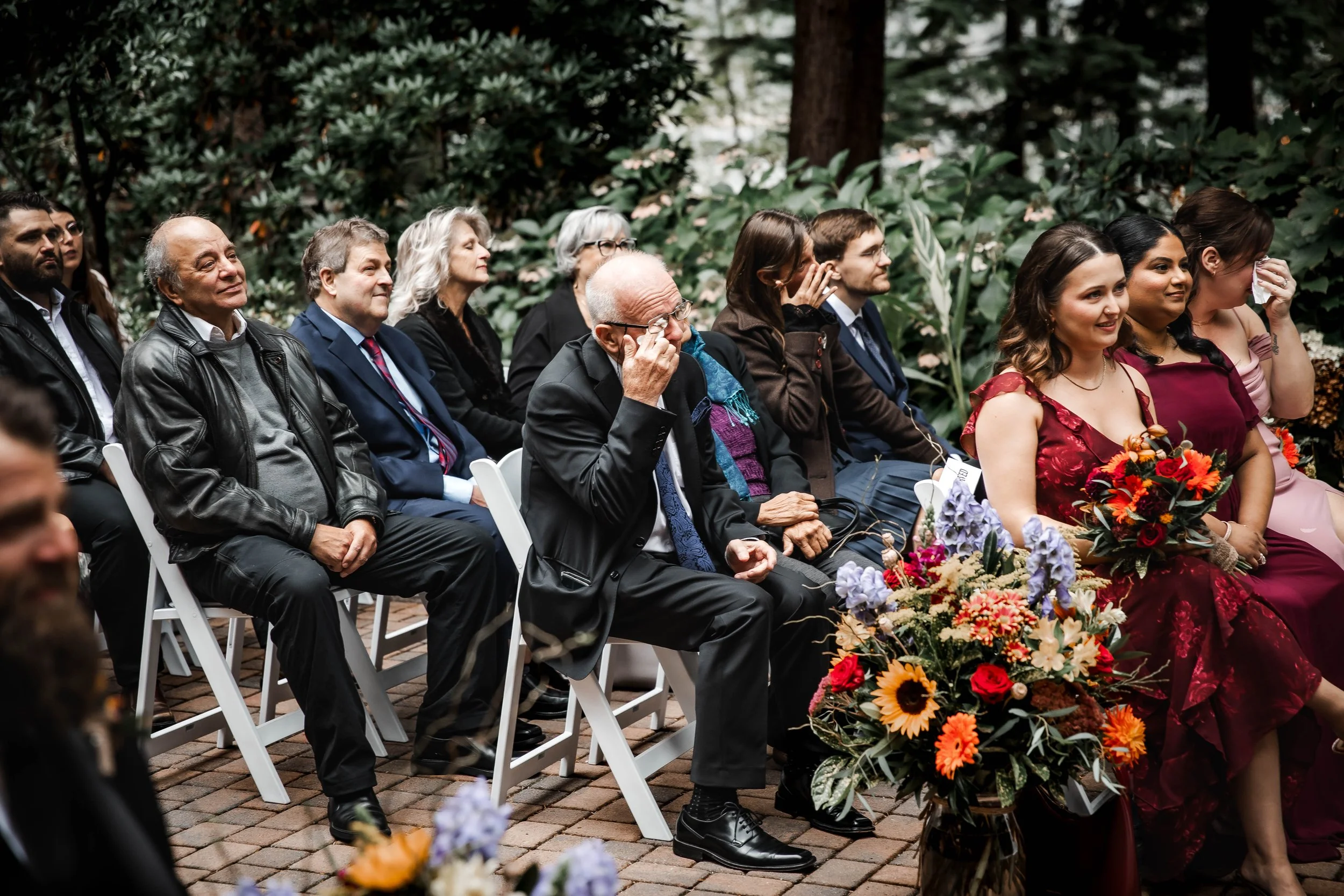 Emotional wedding guests wiping away happy tears during a heartfelt fall wedding ceremony, surrounded by colourful autumn flowers at Whonnock Lake, BC.