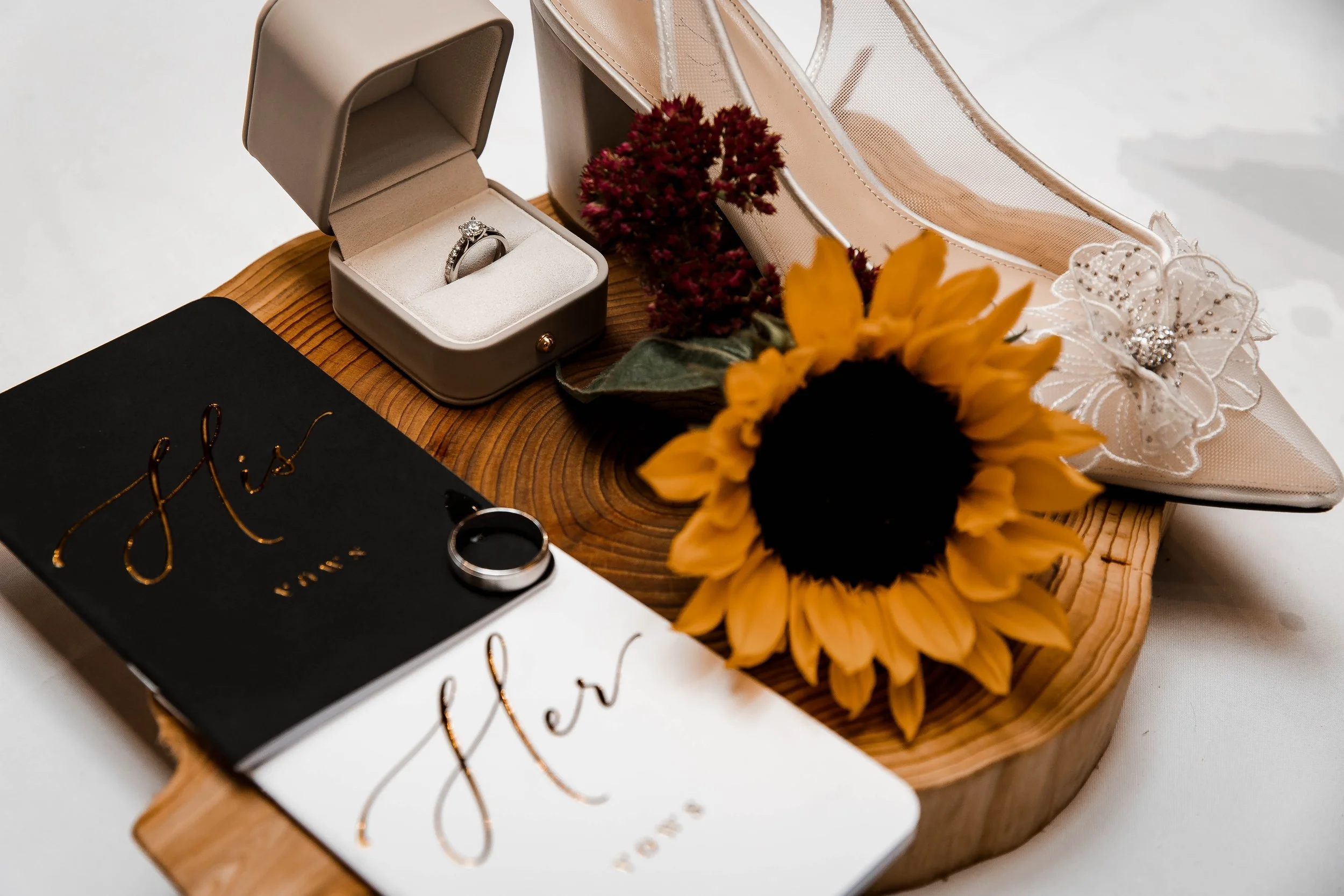 Elegant wedding rings displayed alongside a bright yellow sunflower, burgundy flowers, bridal accessories and personalized wedding details at a fall wedding in Maple Ridge, BC.