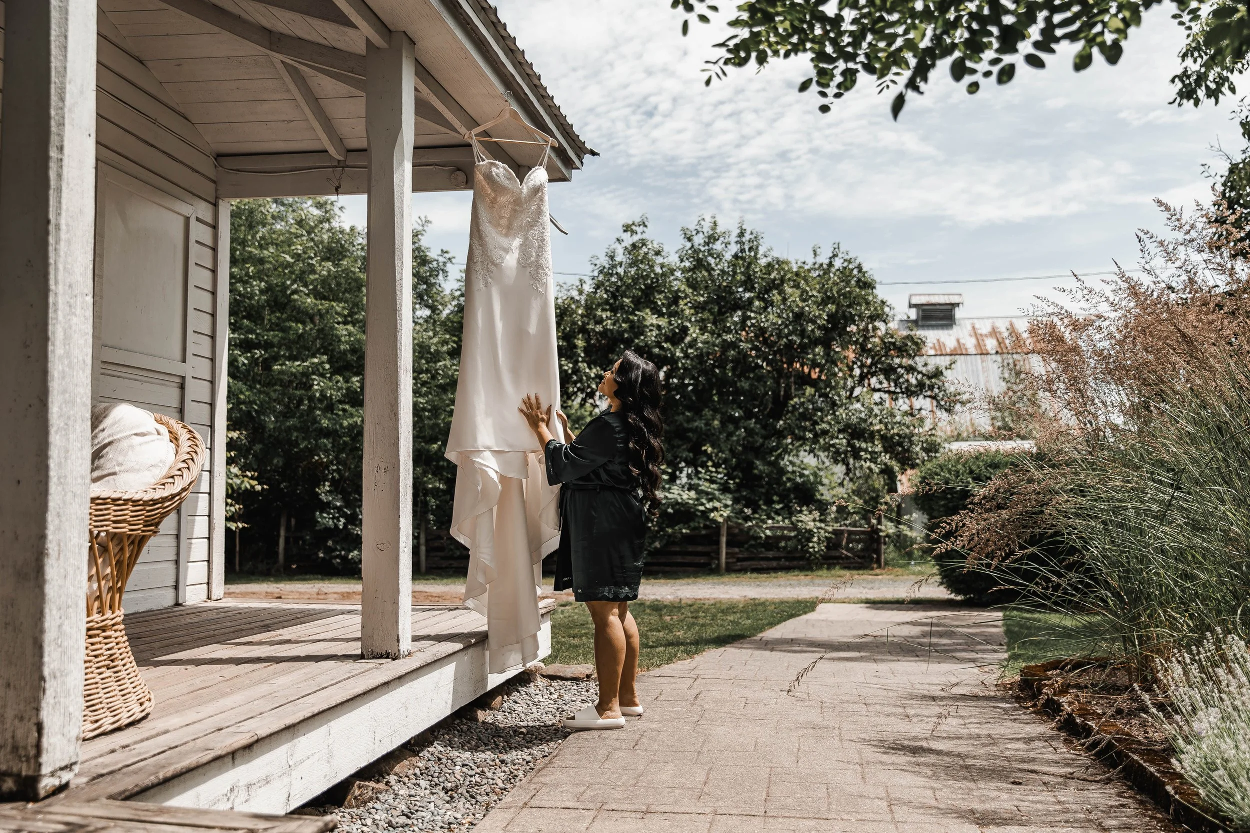 Bride admiring her wedding dress hanging outside a rustic venue during wedding day preparations in the Fraser Valley, BC.