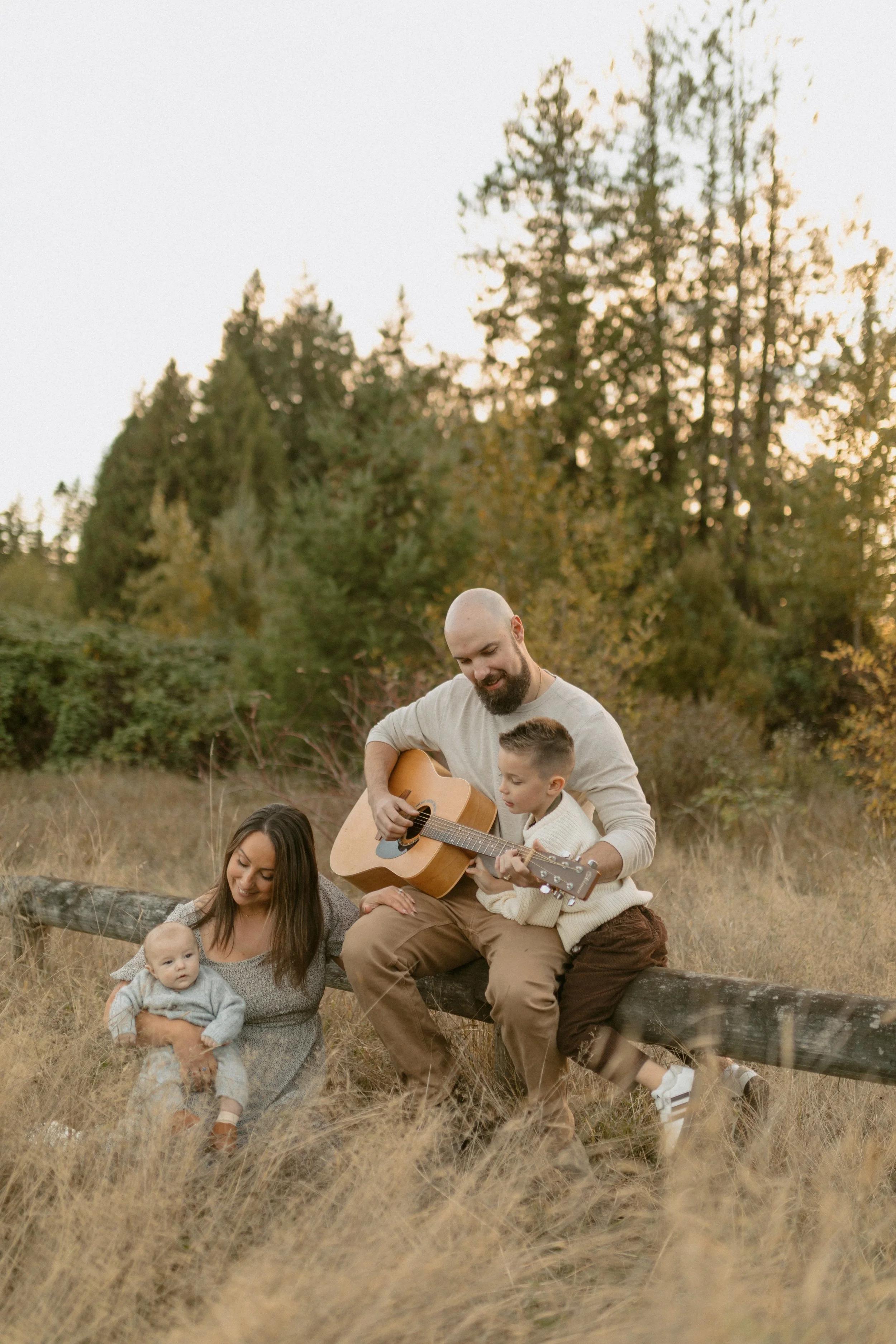 husband and wife photography duo. Man paying guitar and woman with children n golden hour