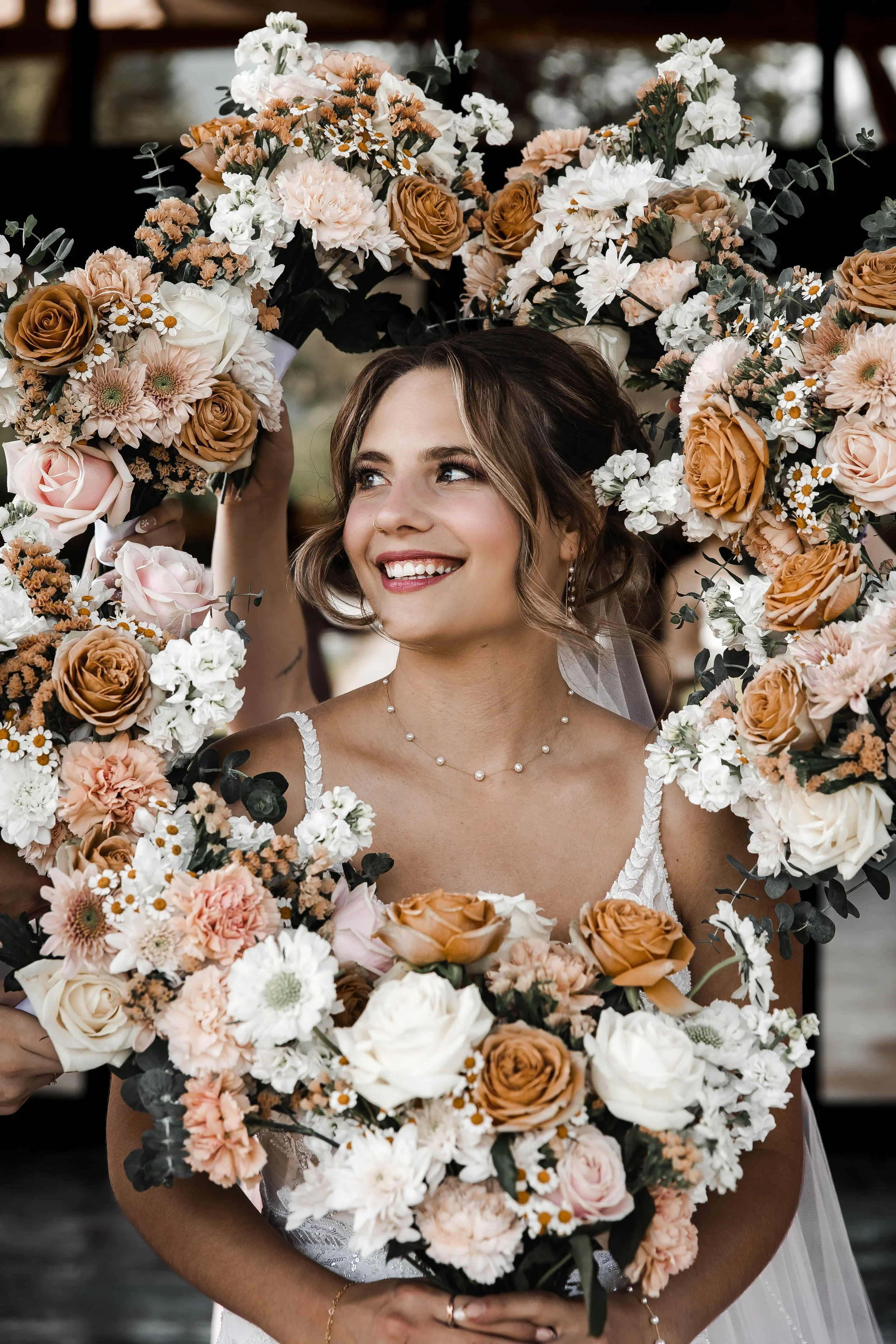 Bride smiling beneath a floral arrangement while holding her wedding bouquet at Bridlewoods.