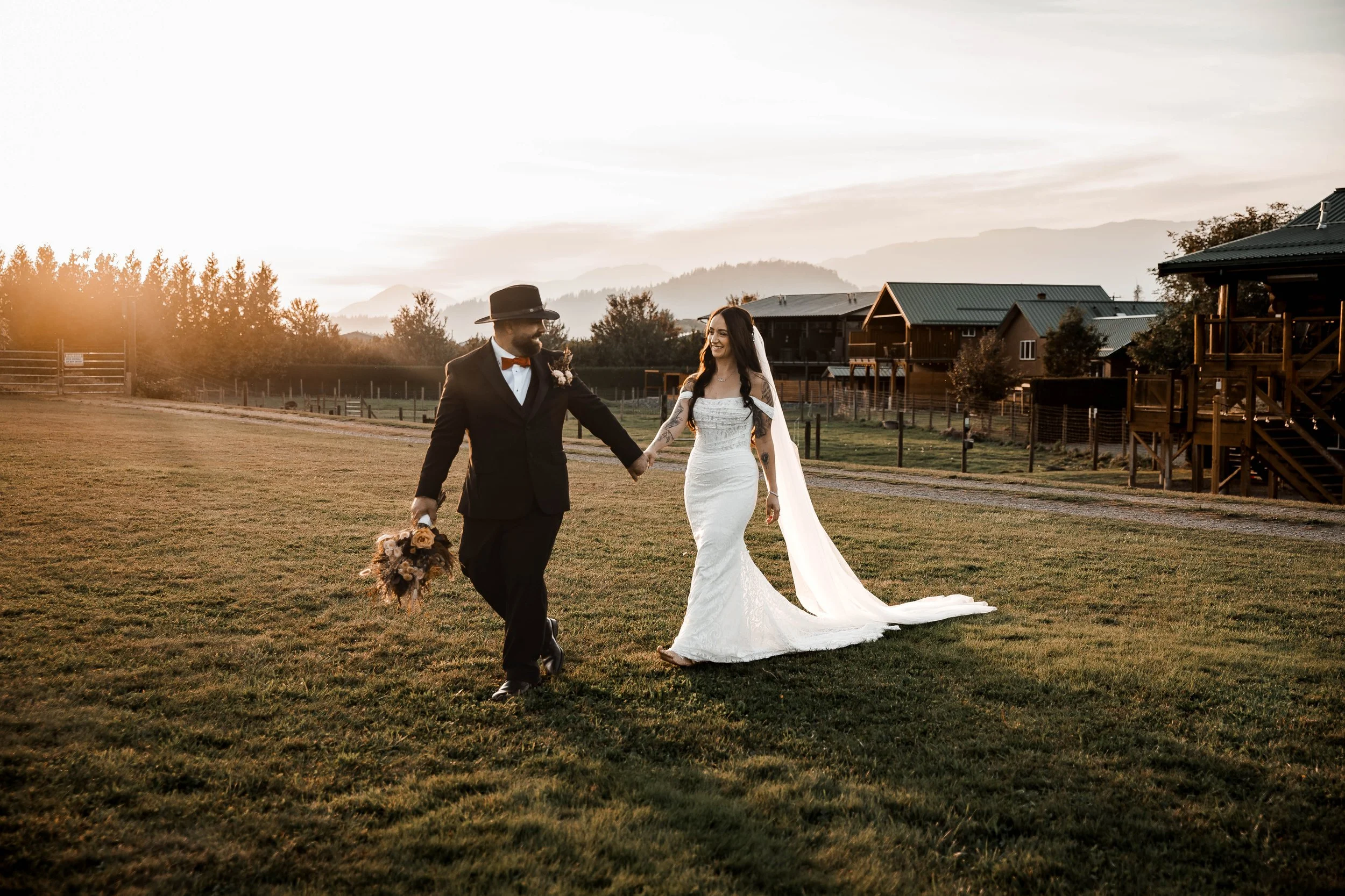 Newlyweds holding hands during golden-hour wedding portraits at Fraser River Lodge in Agassiz, BC, with mountains in the background.