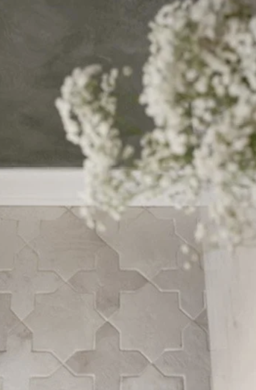Close-up of white baby's breath flowers in a transparent vase near a tiled wall with a geometric pattern.