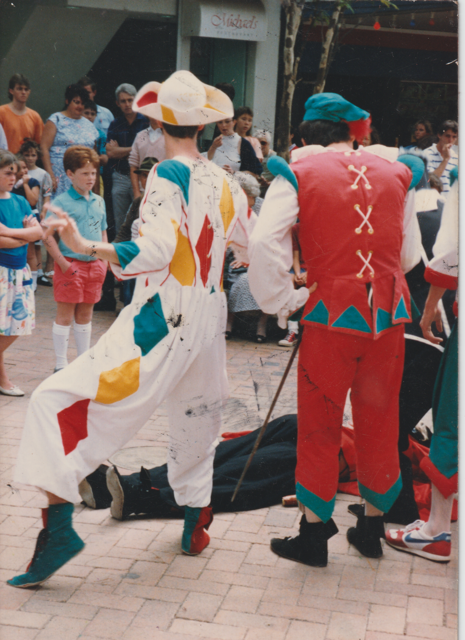 Clown performers in colorful costumes entertaining children and adults in an outdoor setting.