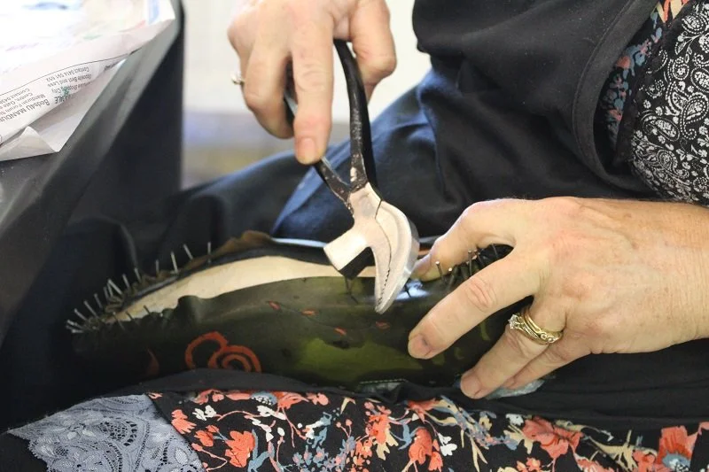 Person working on lasting a shoe using pliers while sitting down.
