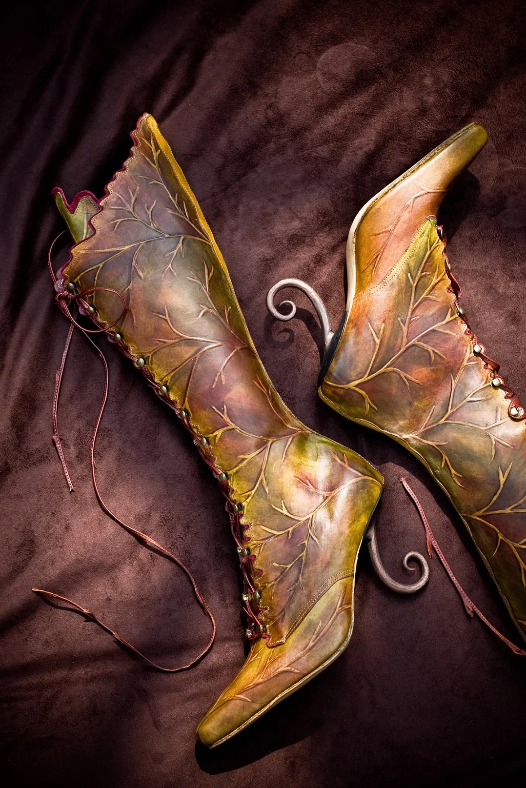Decorative butterfly-shaped shoes with leaf-patterned wings and metallic accents, placed on a dark fabric background.