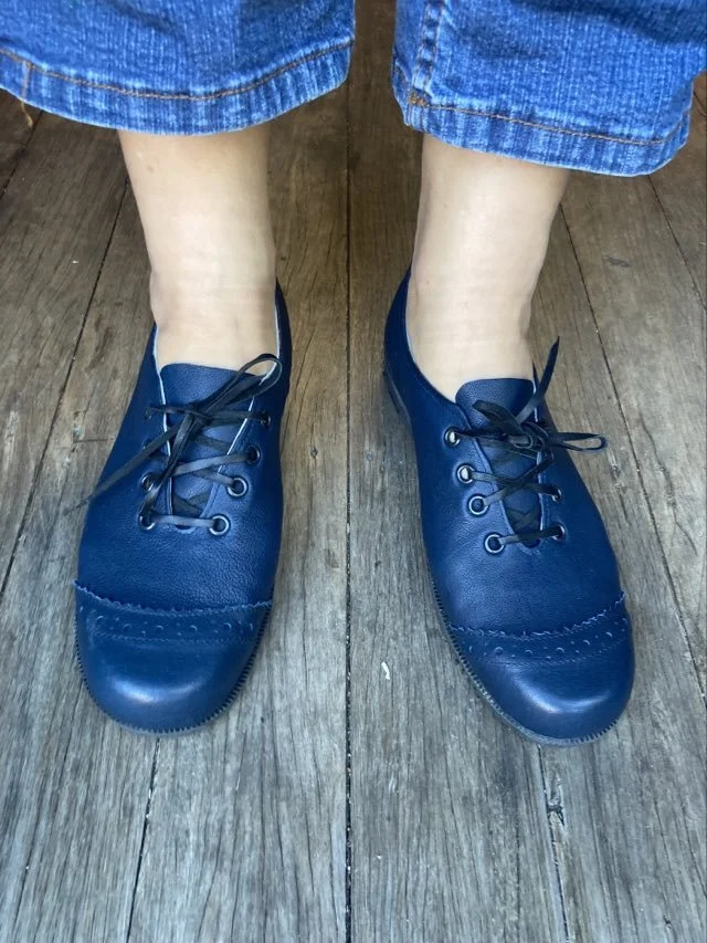 Person wearing blue shoes and rolled-up blue jeans standing on wooden floor.