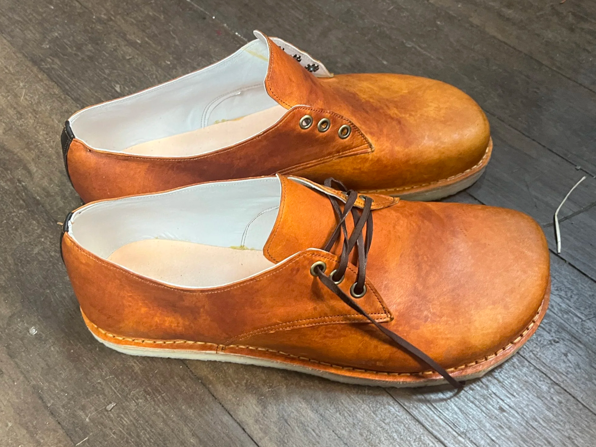 A pair of brown leather shoes on a wooden floor, viewed from above.