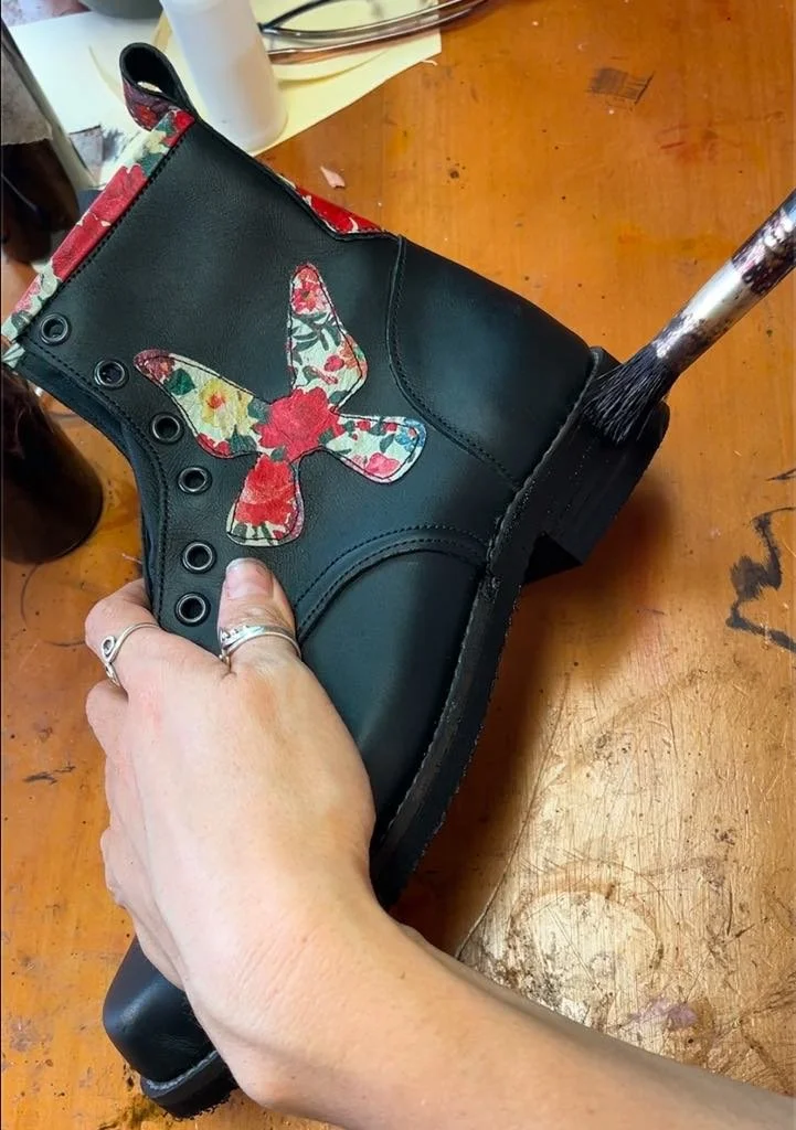 Putting the finishing touches on a pair of handmade black leather ankle boots with a floral butterfly design on the side made in our 5-day boot making course