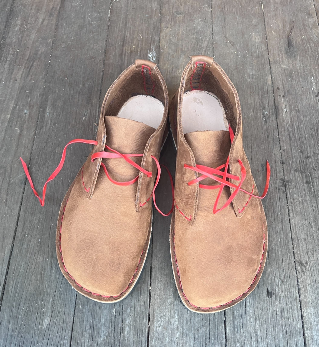 Pair of tan suede leather boots with red laces on a wooden floor.