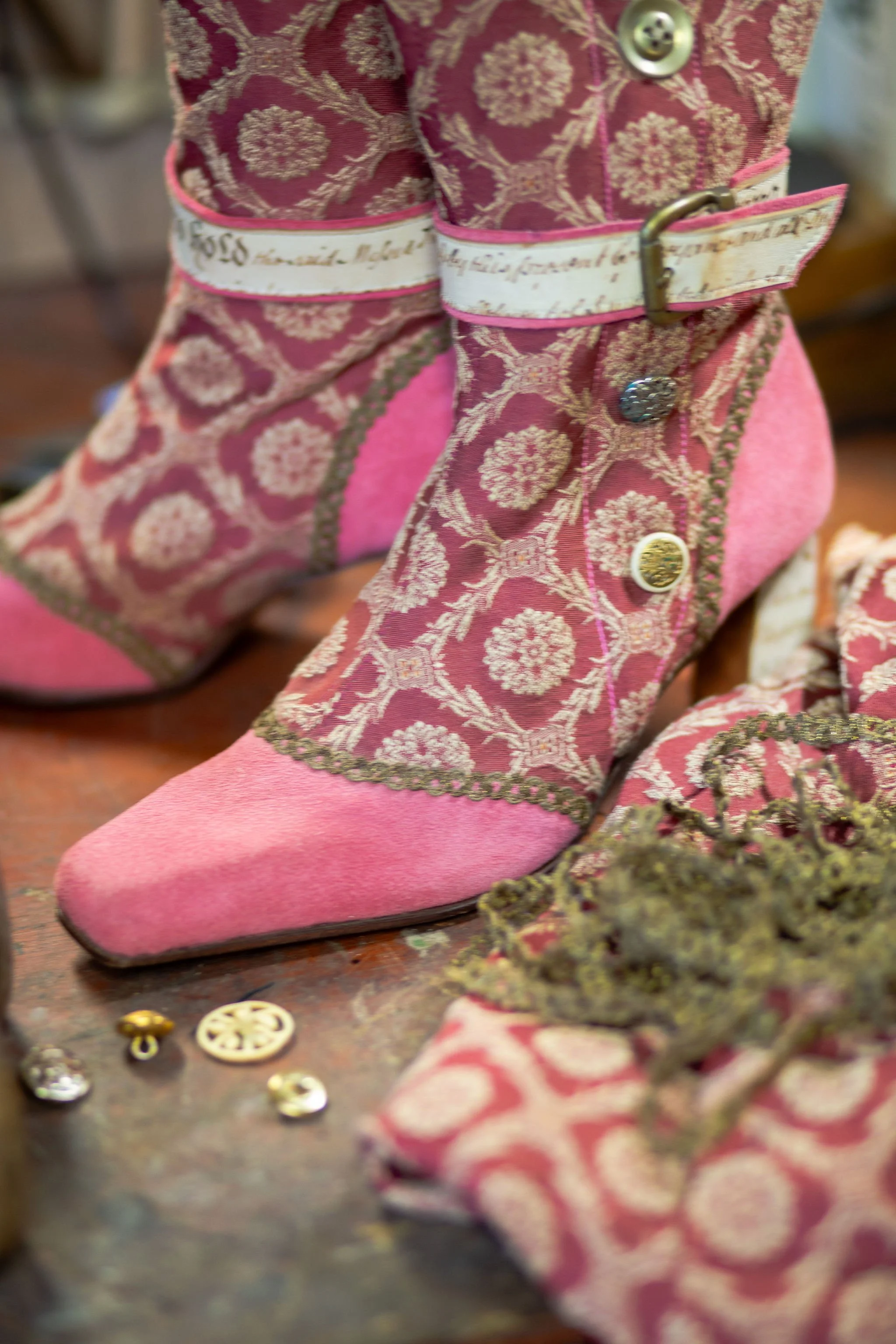 Pink Victorian-style children's dress with gold trim, buttons, and a belt, displayed with jewelry and small decorative objects on a table.